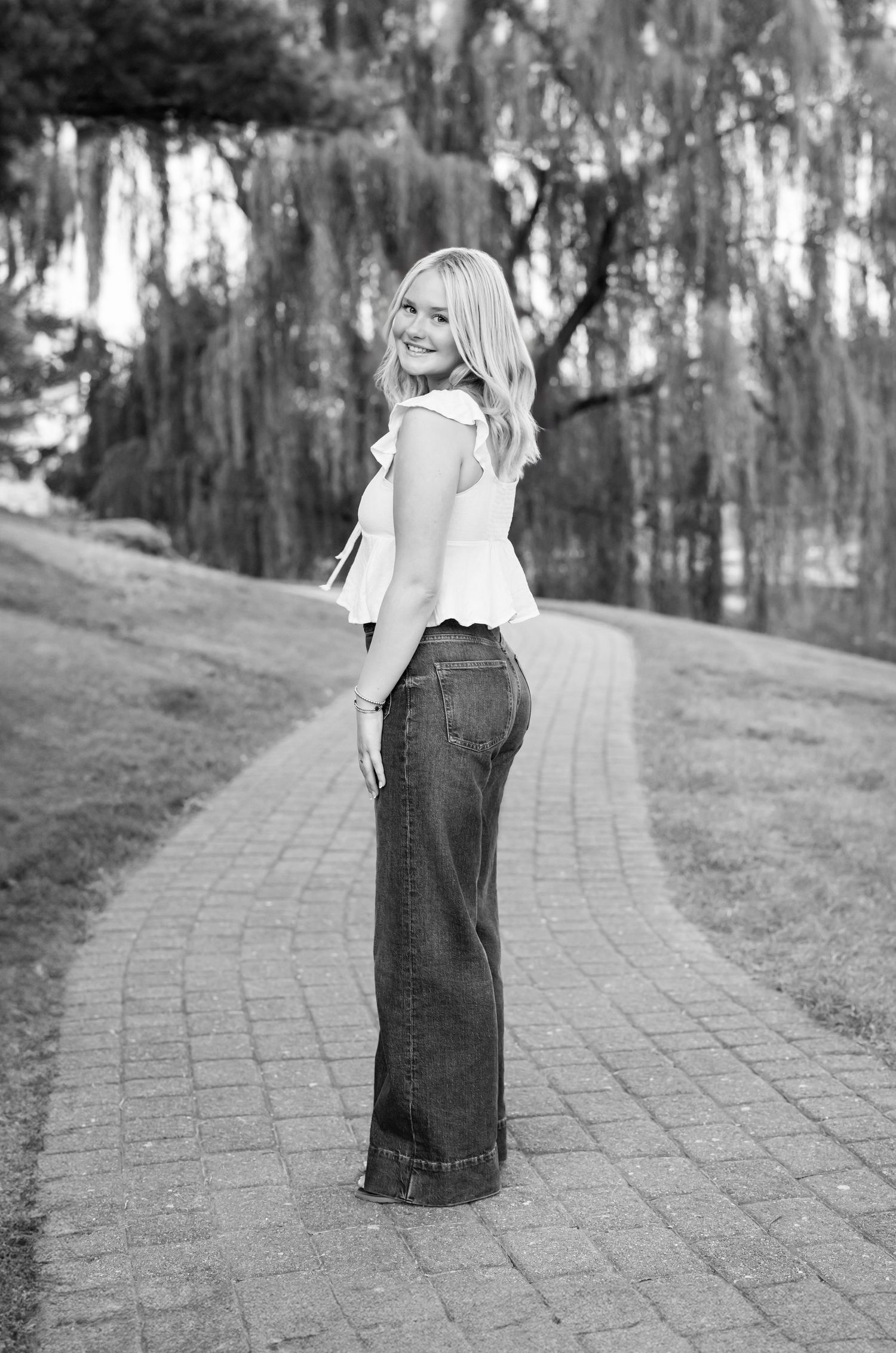 Black and white photos show a high school senior girlin a flowing dress walking along a curved stone path through a wooded area.