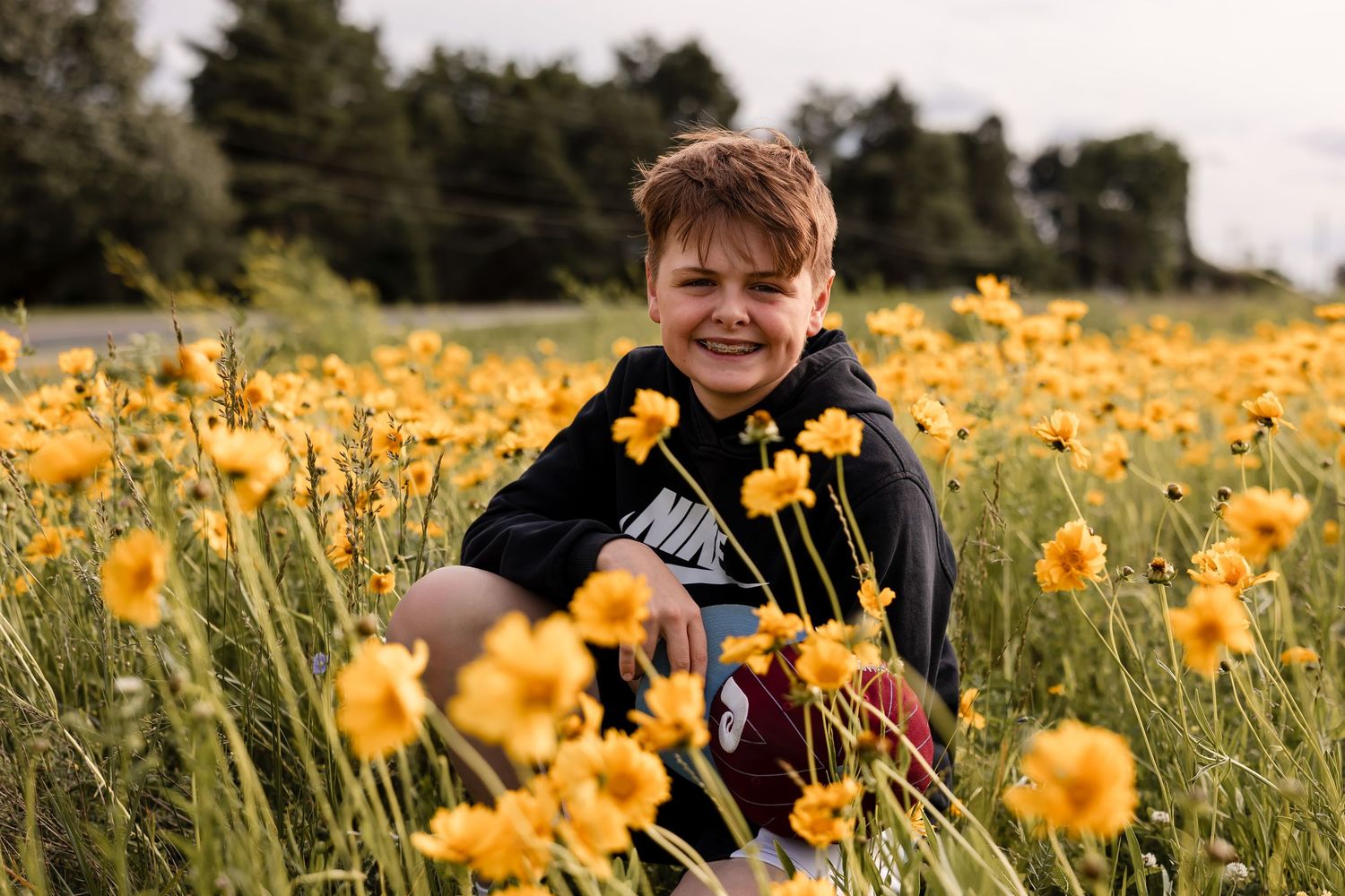 A senior portrait of a young man among yellow wildflowers blooming in a green meadow on a sunny summer day.