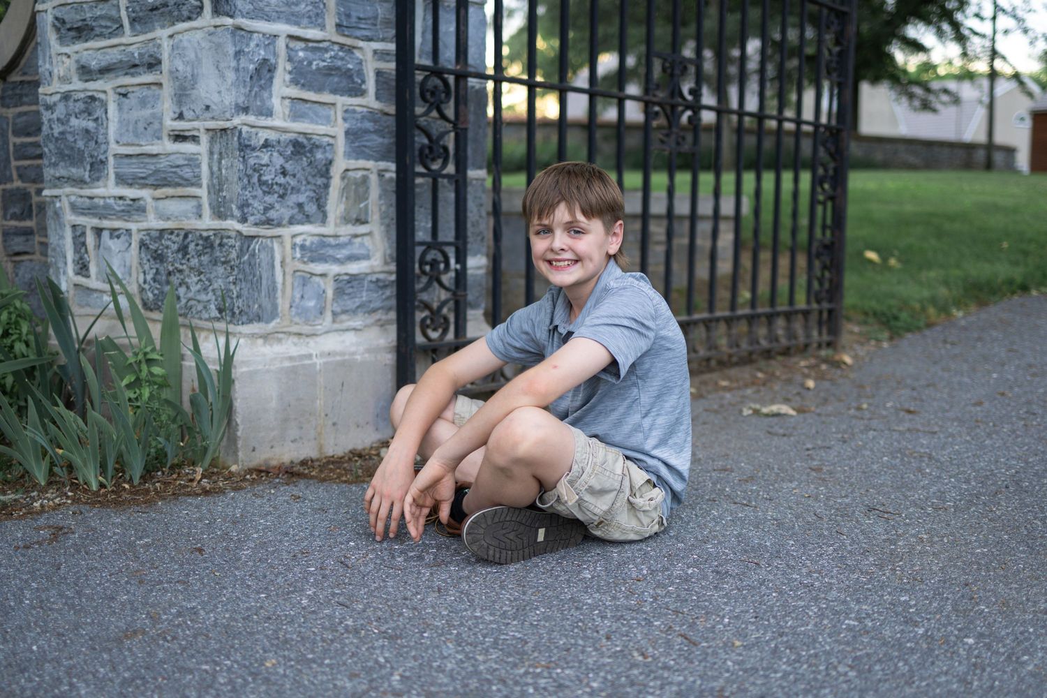A teen boy sits beside stone wall and iron fence at Donegal Presbyterian Church in Mount Joy, PA during family photo session.