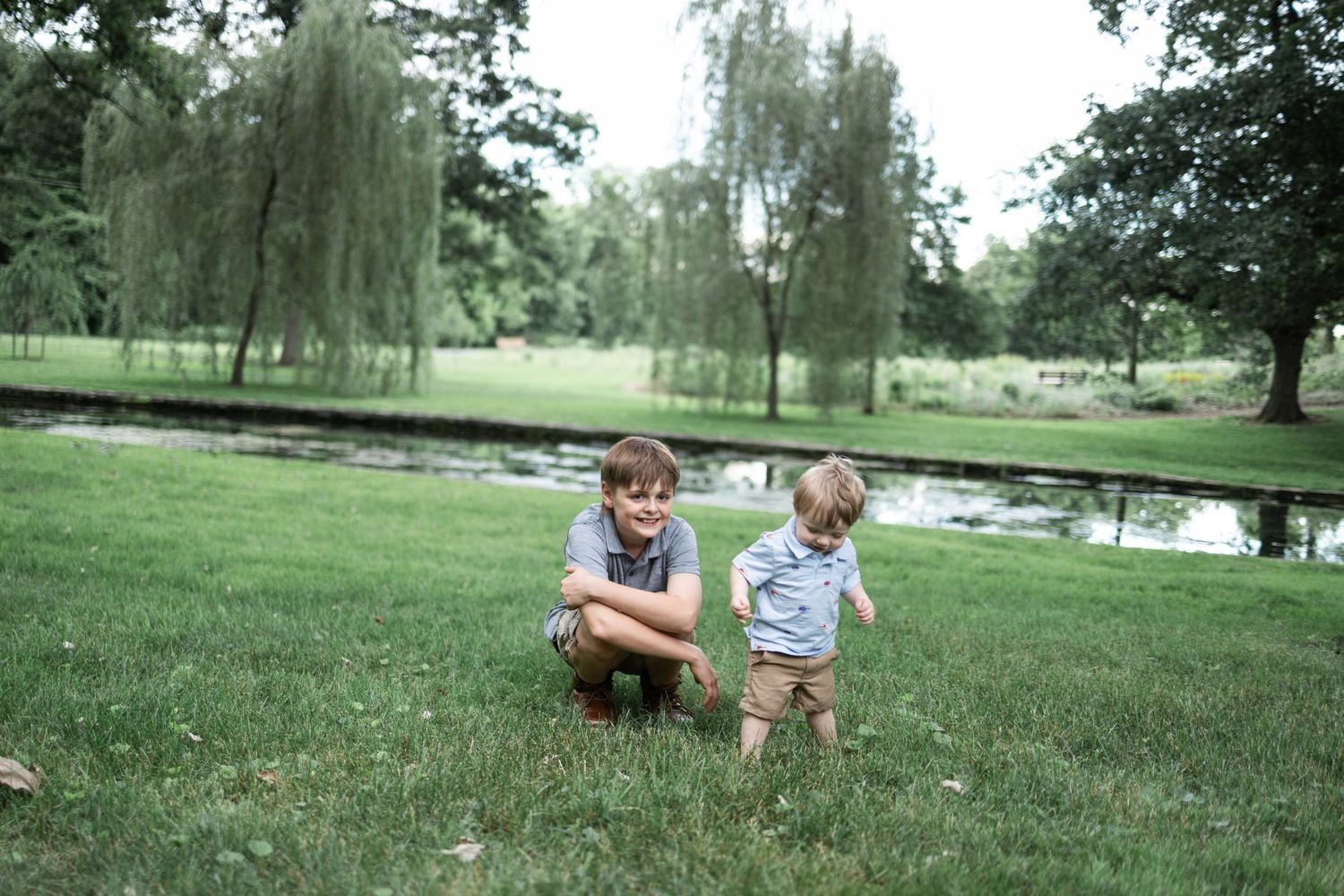 A teen boy squats in grass with toddler boy at Donegal Presbyterian Church in Mount Joy, PA during a family photography session.