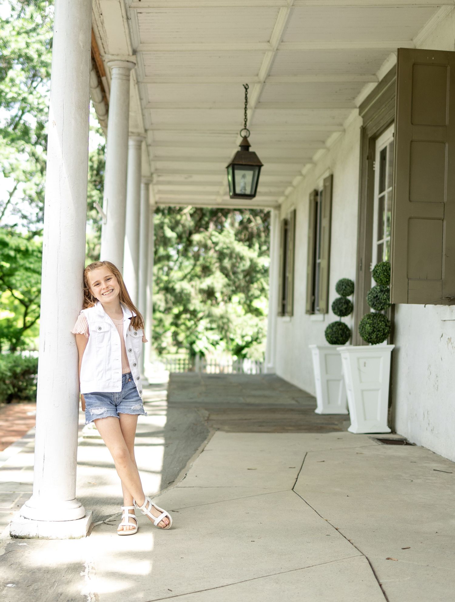 A young girl leans on a porch column at White Chimney Estates in Gap, PA during a family photo session.