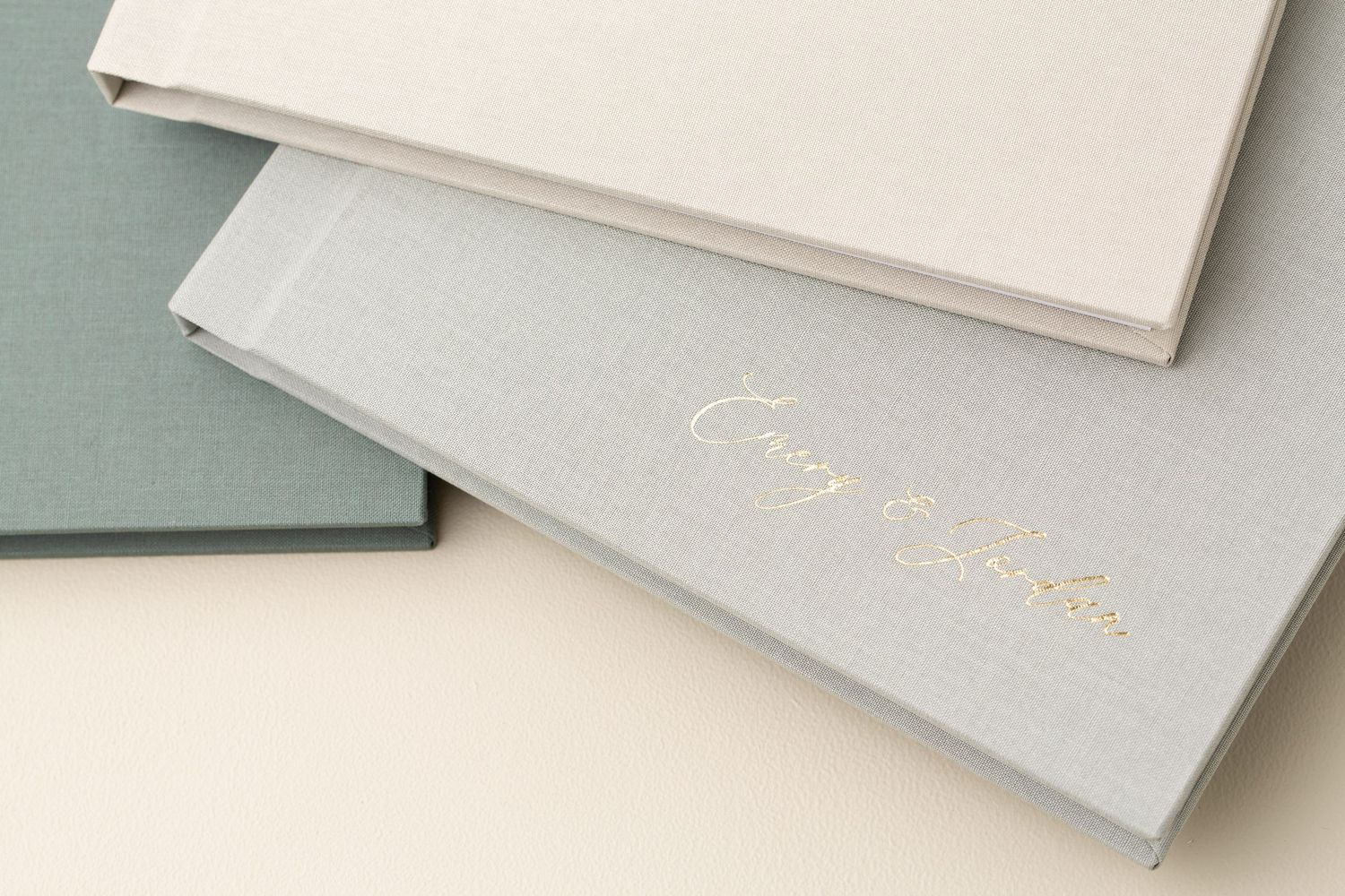 Three linen heirloom photo albums in sage, cream, and grey, custom designed for senior portraits and family photography in Lancaster, PA.