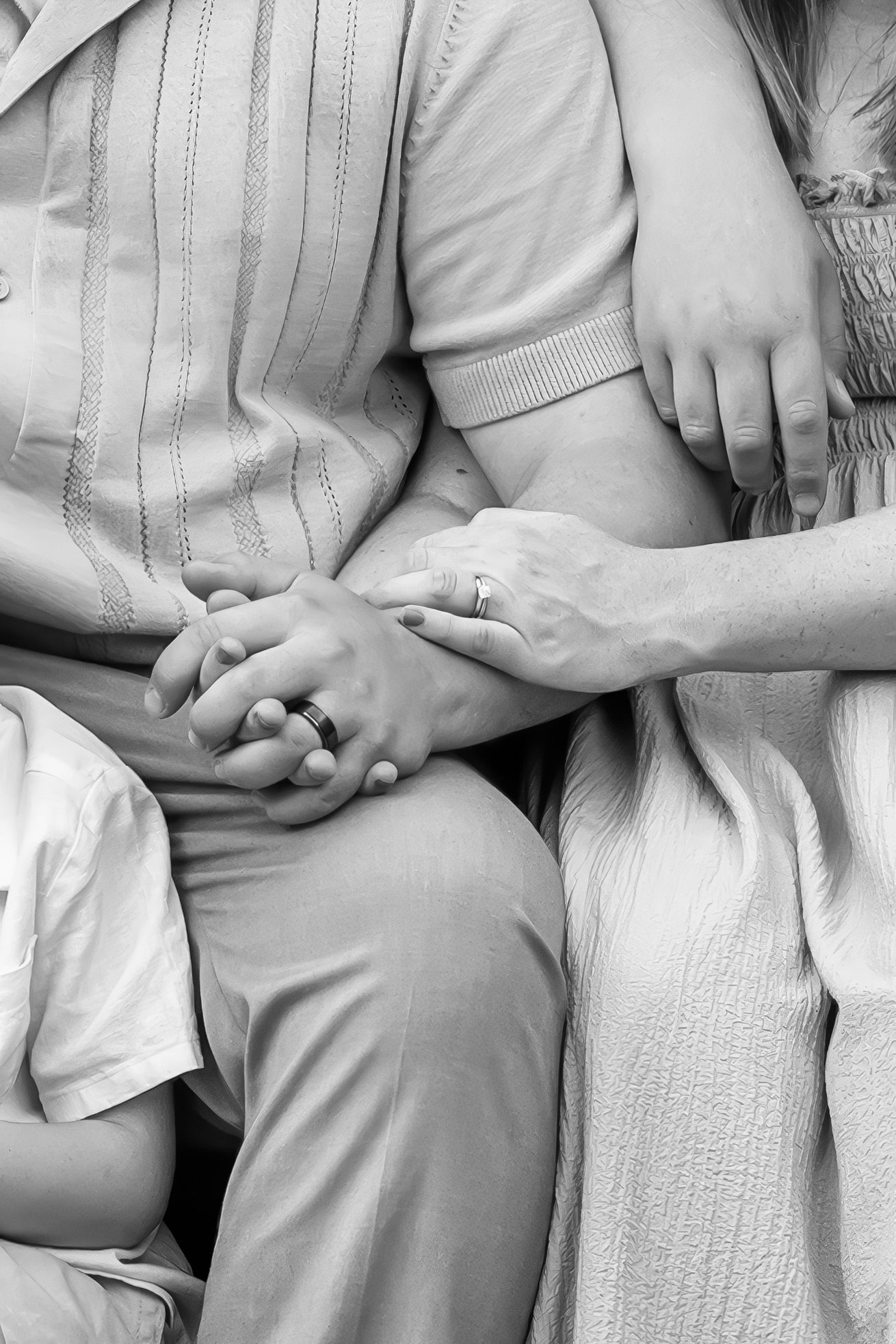 Black and white photo of a family sitting together, hands clasped, wearing wedding rings, showing love and togetherness.