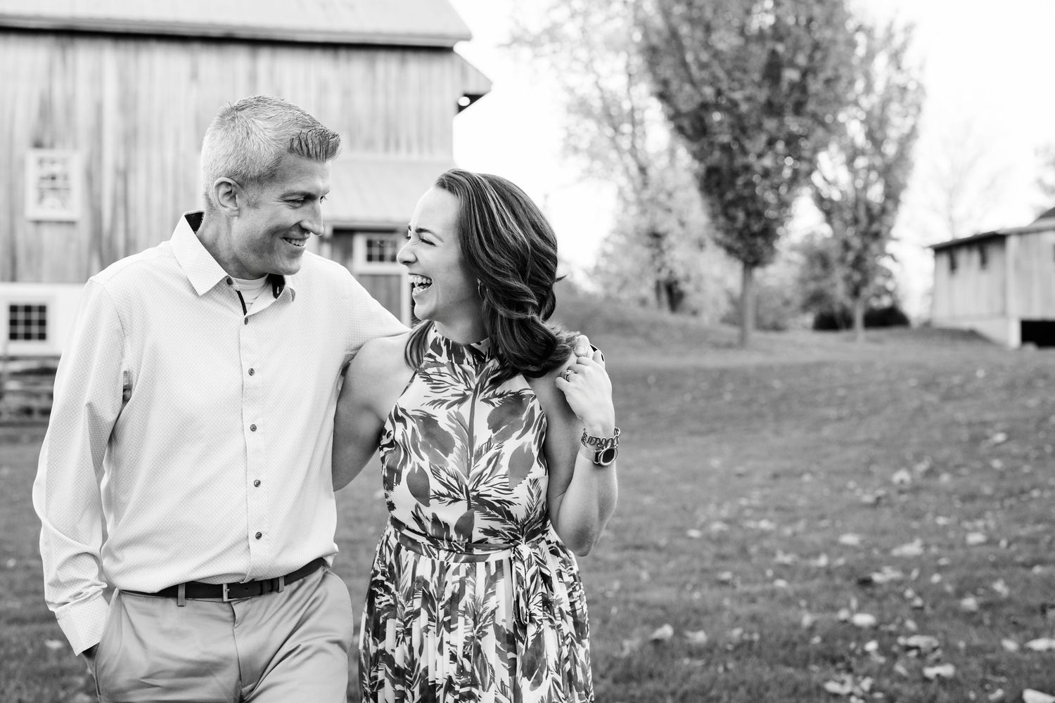 Black and white photo of a smiling couple walking together outdoors near a rustic barn on a farm.
