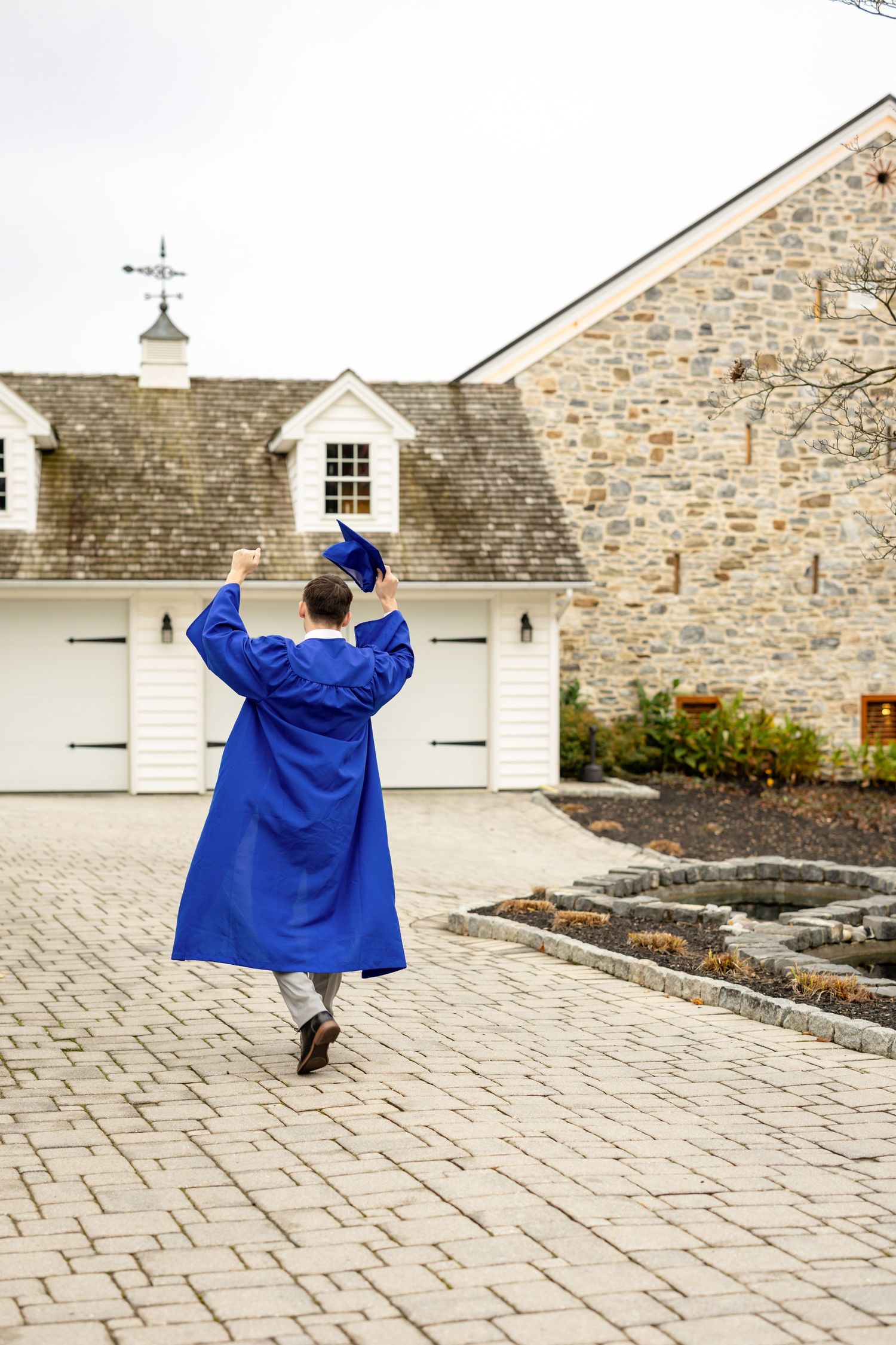 A high school graduate walking in his gown holding his cap in the air.