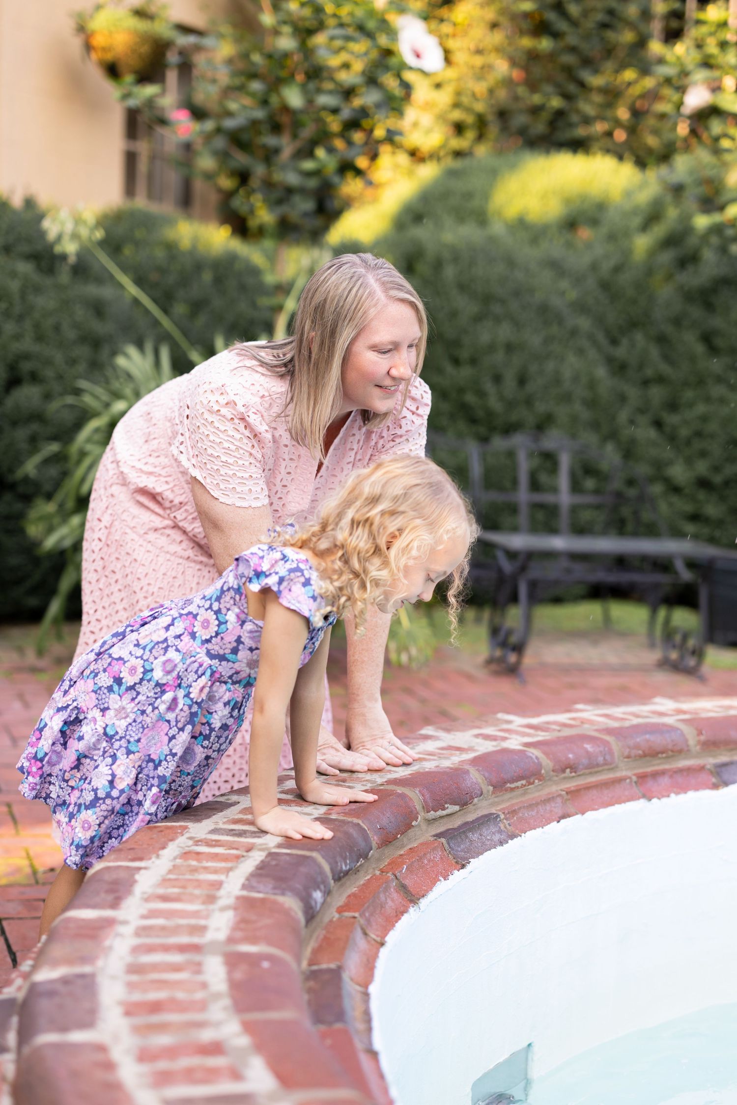 Authentic family photo of mother and daughter leaning over fountain feature in a lush garden, by Megan Mariah Photography, Lancaster, PA.