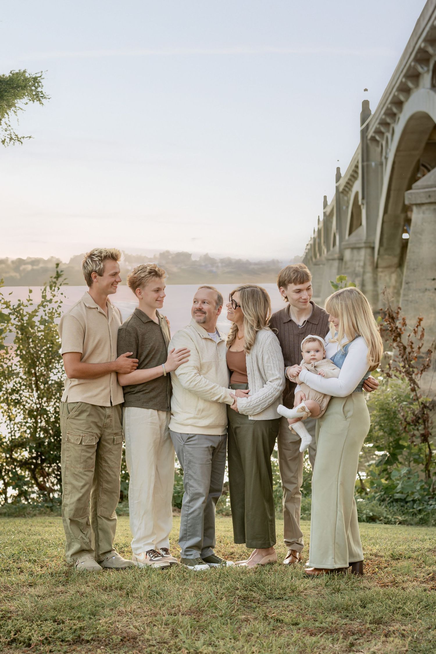 A group of people dressed in neutral tones gather together for outdoor family photos in a golden sunset setting.