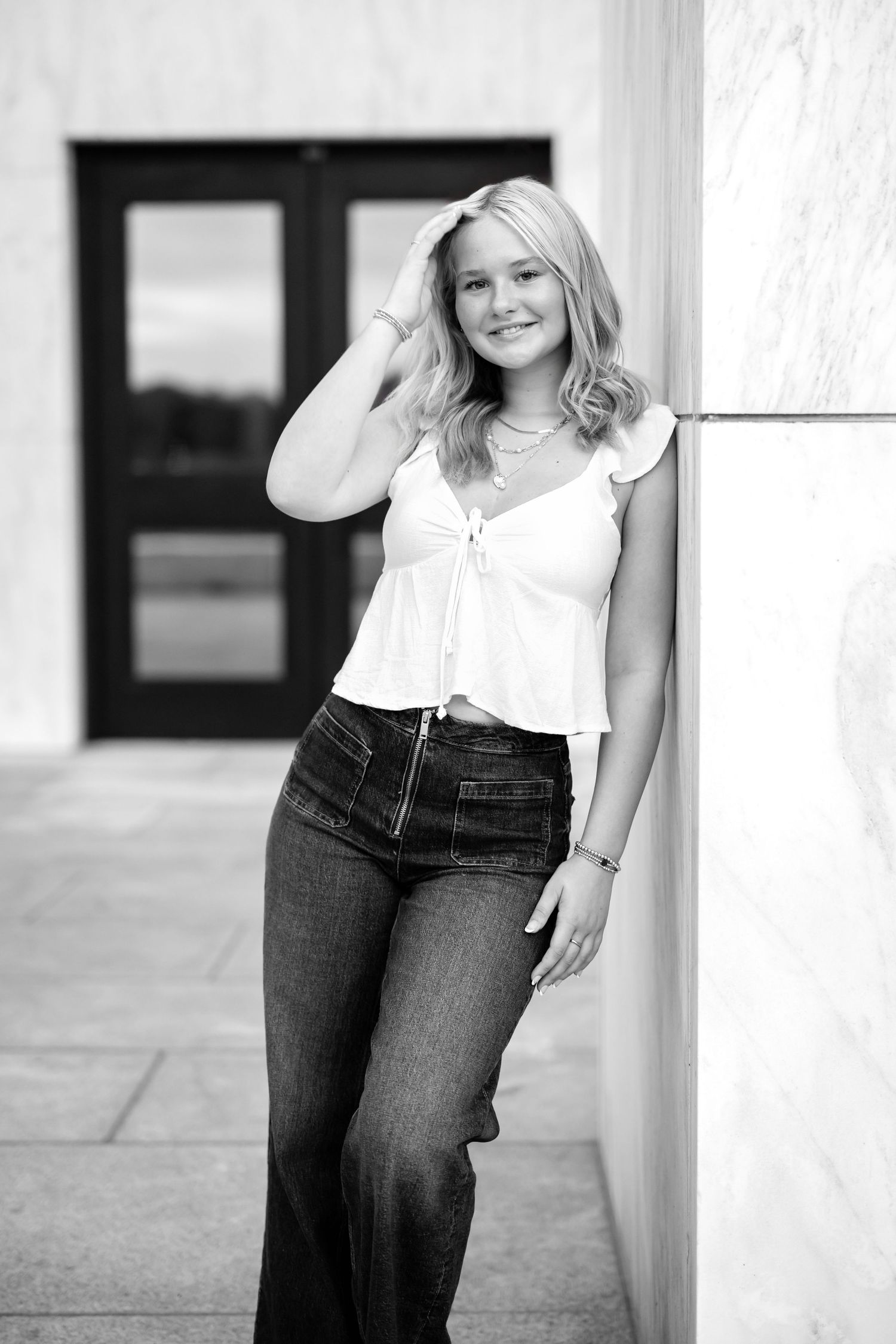 A black and white portrait series showing a high school senior girl in casual attire posing against a white wall.