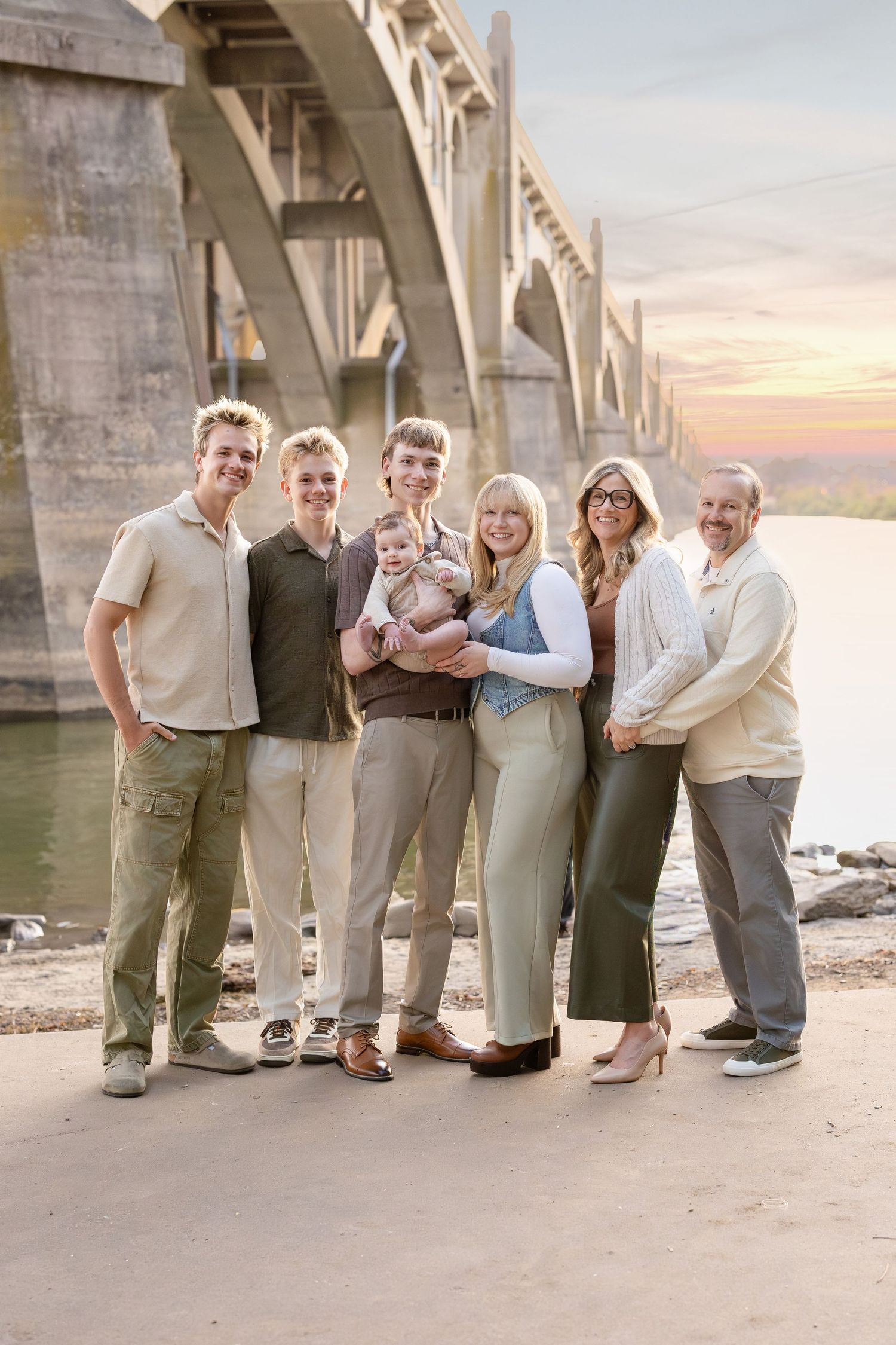 A group of people standing together near a bridge during a sunset.
