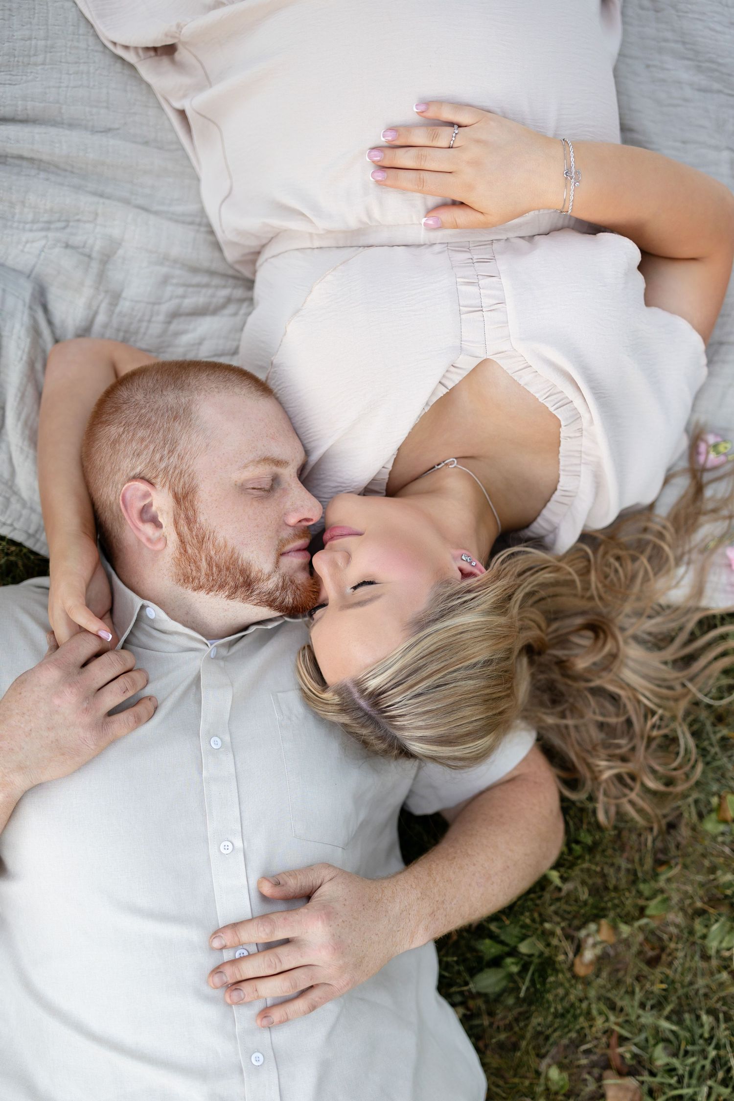 Couple lying on a blanket outdoors, sharing a romantic moment, man with red beard embracing blonde woman.