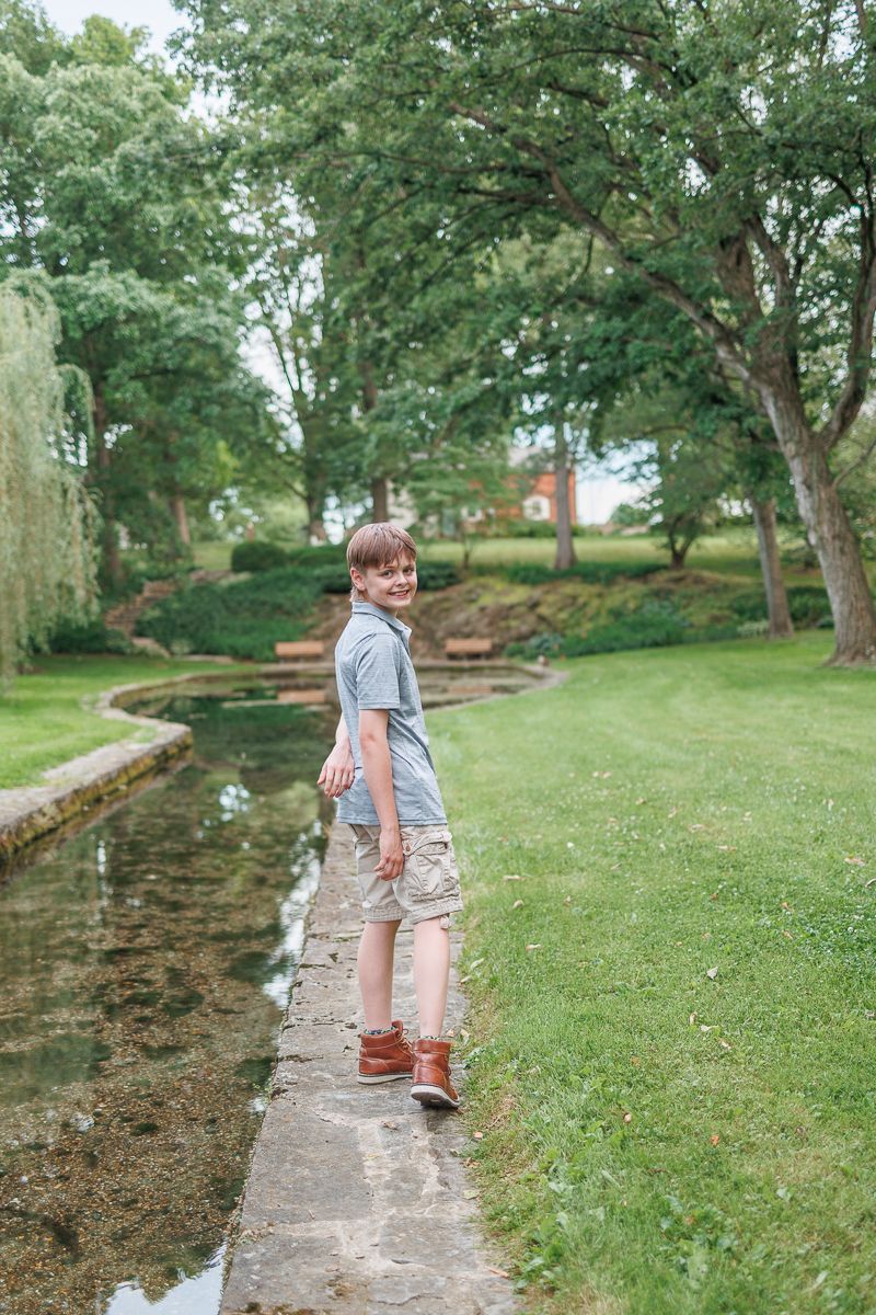 teen boy poses beside water feature at Donegal Presbyterian Church in Mount Joy, PA during family session with Lancaster, PA photographer