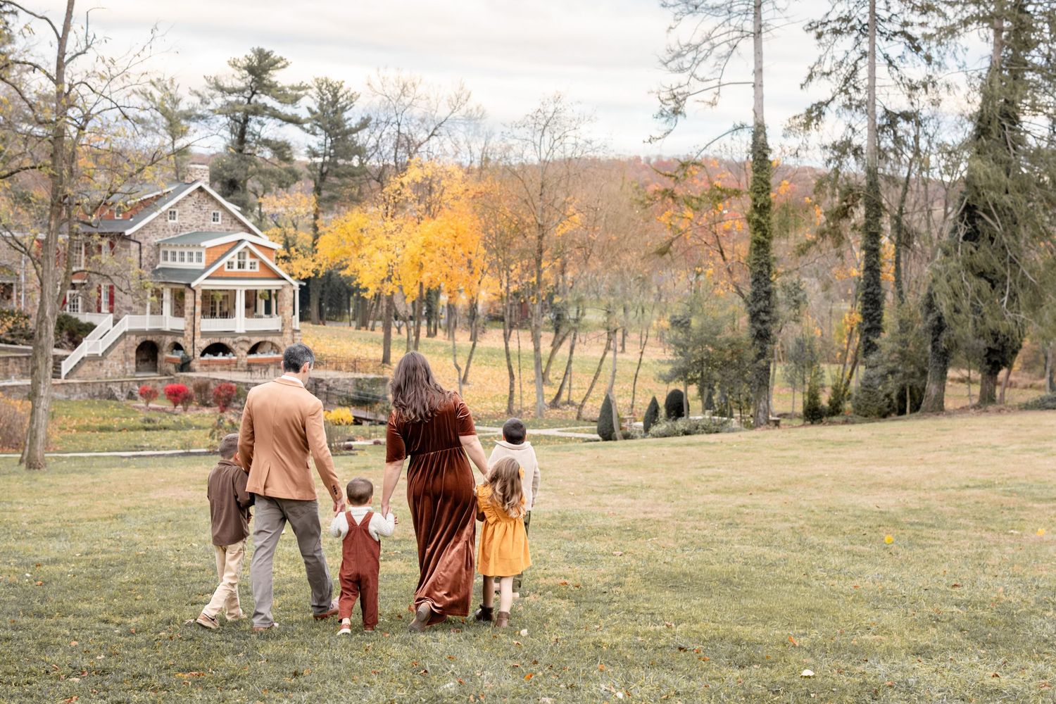 Family walking together on green lawn toward a charming house with autumn foliage in background.