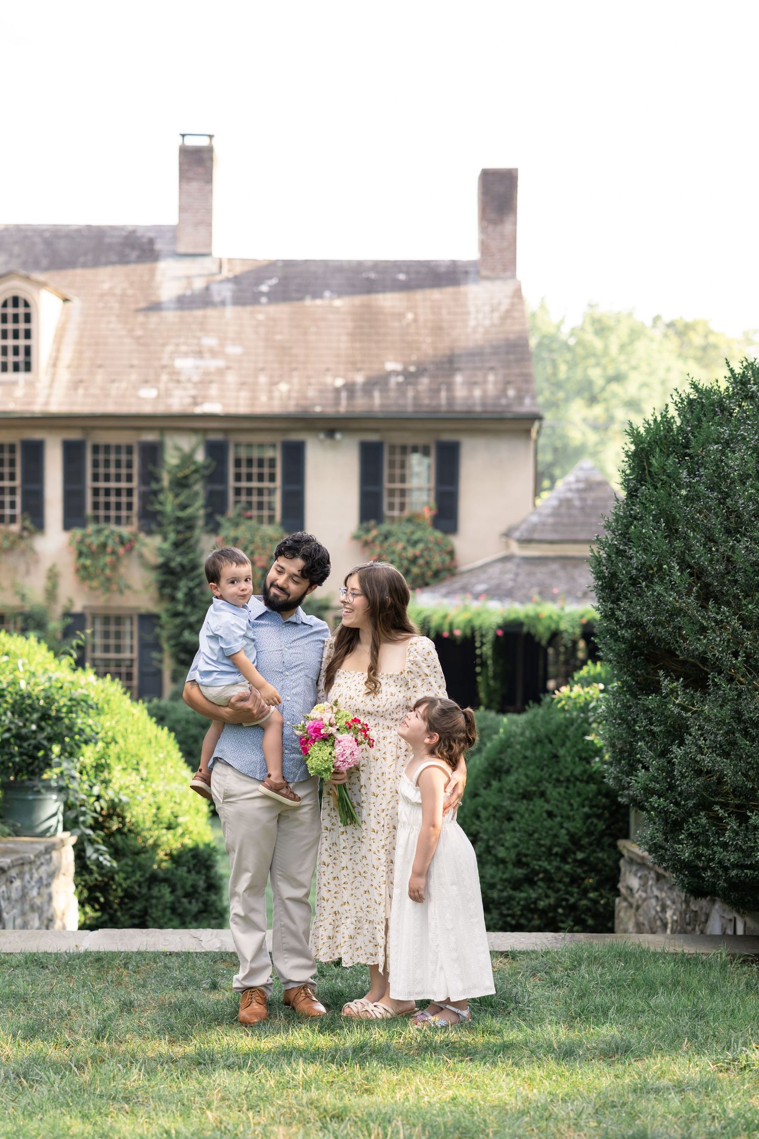 Family enjoying a sunny afternoon together on a manicured lawn in front of a beautiful stone mansion.