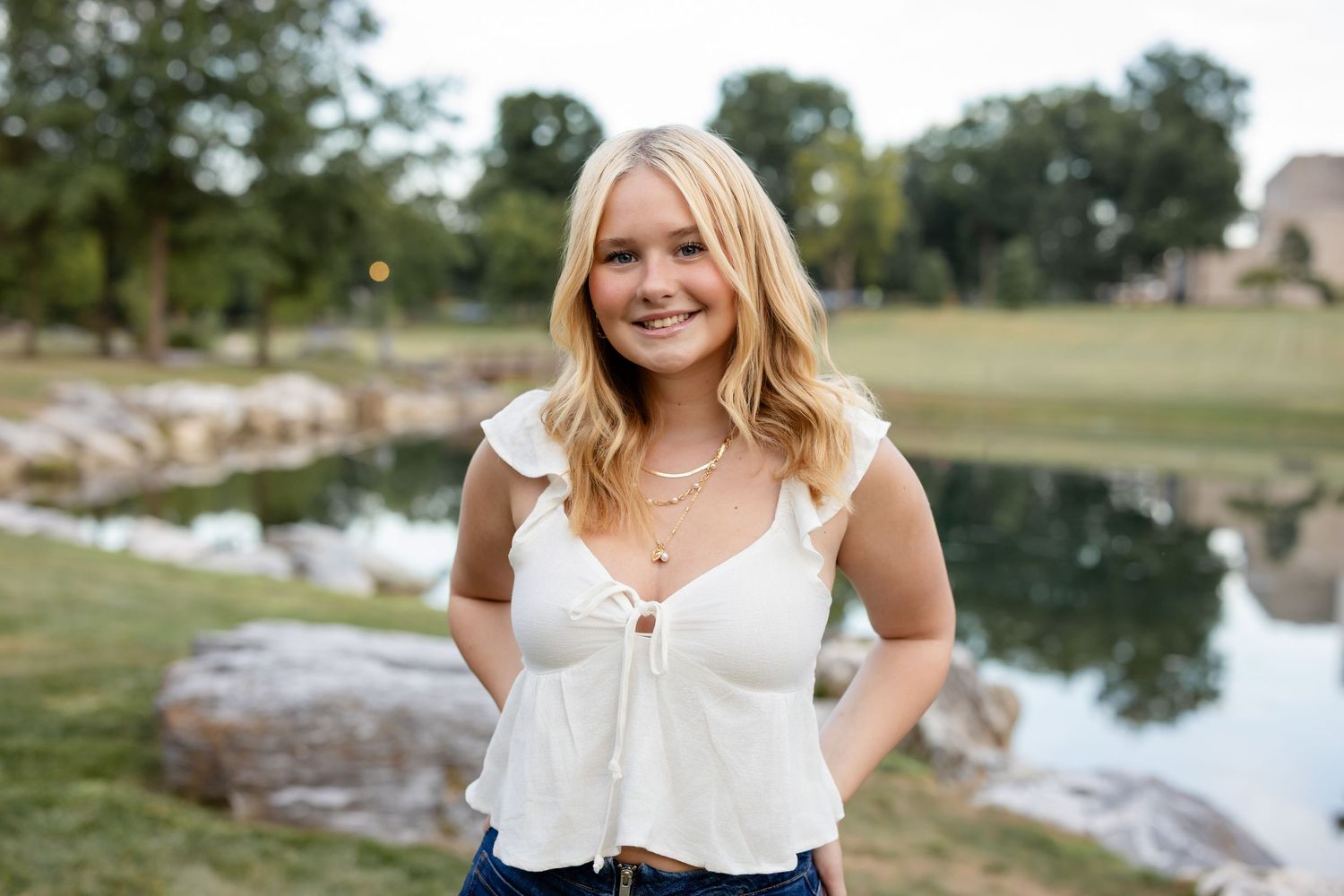 High school senior portraits of a blonde girl taken near a lake with natural lighting and greenery in the background.
