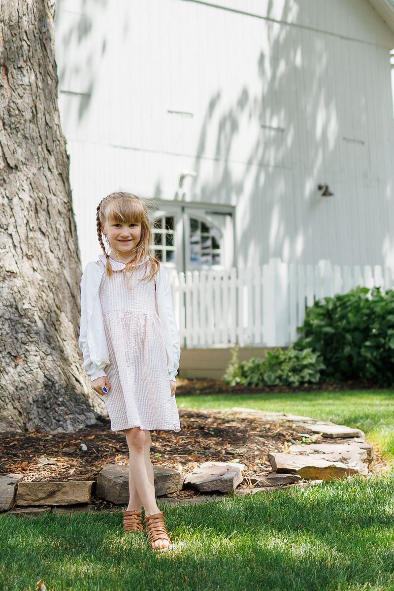 A young girl in a pink dress stands in front of a white barn at White Chimneys Estate in Gap, PA during a family photography session.