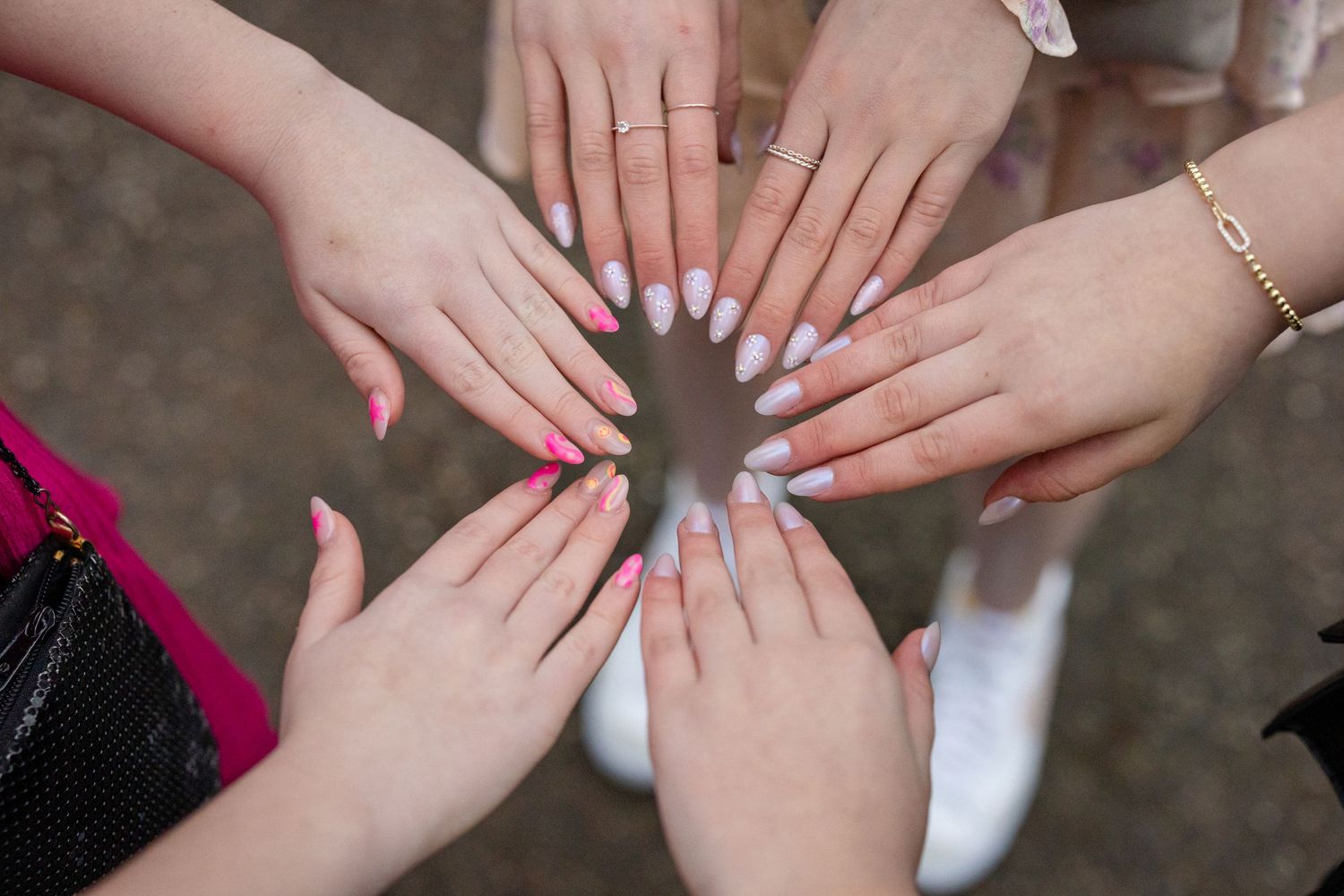 Six hands with different nail polish colors and styles arranged in a circle to show off manicured nails.