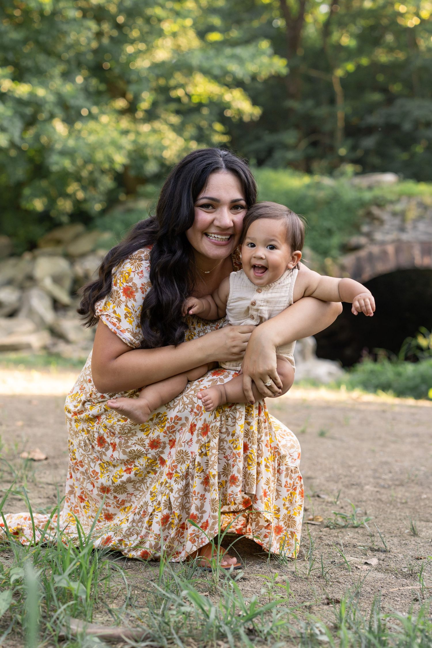 A heartwarming summer family photo of mother and baby outdoors on a sunny day near a stone bridge, by Lancaster, PA photographer.