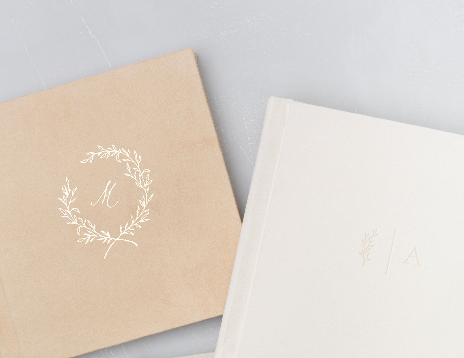 Two elegant wedding albums with monogram designs in beige and white.