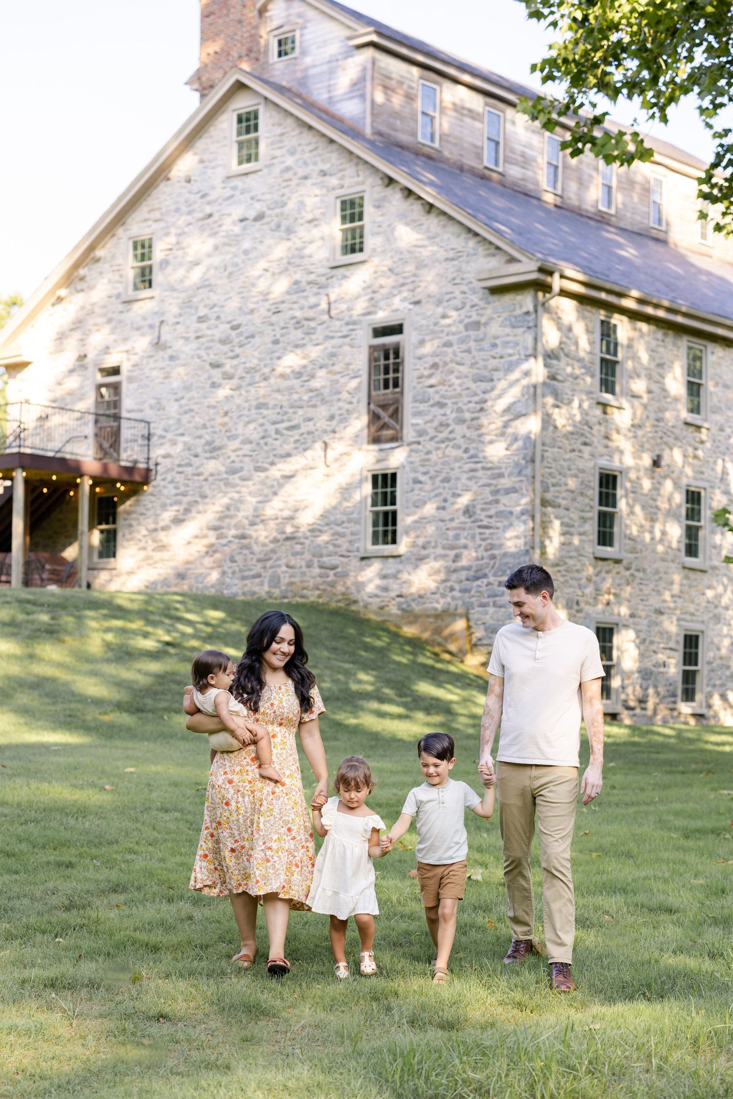 A happy family of five walks on green grass in front of a historic stone building on a sunny day.