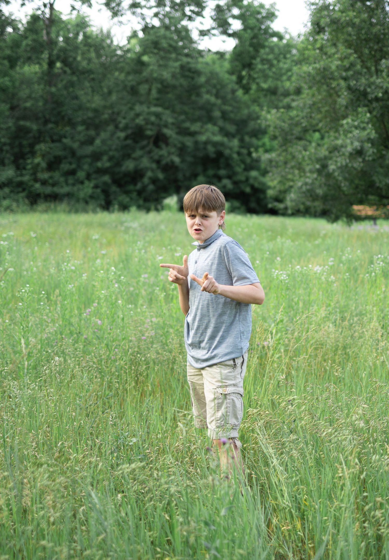 A teen boy stands in a tall grassy meadow wearing a gray t-shirt and khaki shorts during a family photo session, Mount Joy, PA.