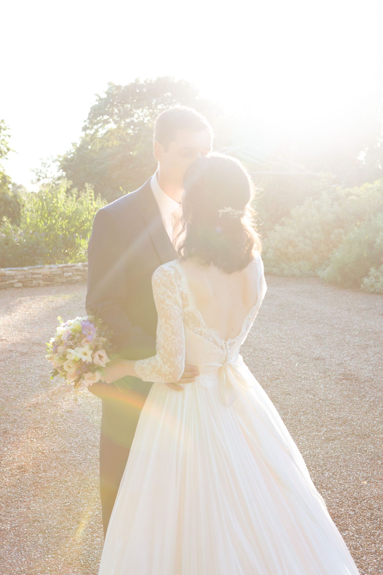 A couple in a romantic wedding pose backlit by golden sunlight at The Farm at South Cove, with the bride wearing a lace-backed white gown.