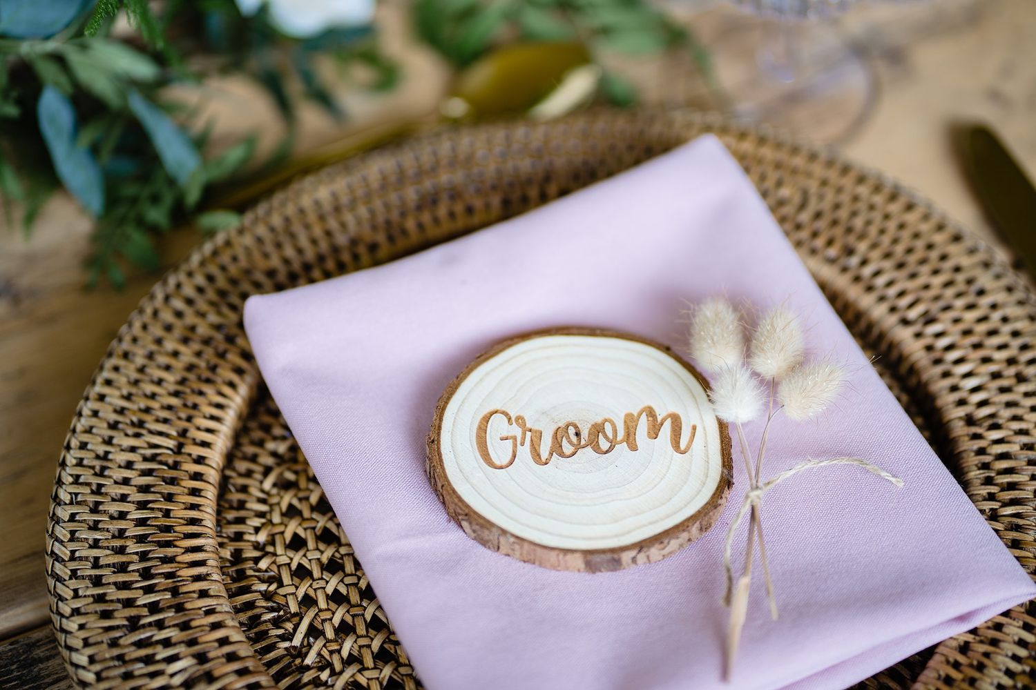 A rustic 'Groom' name card with gold lettering rests on a lavender napkin atop a woven charger plate in Lunenburg wedding venue.