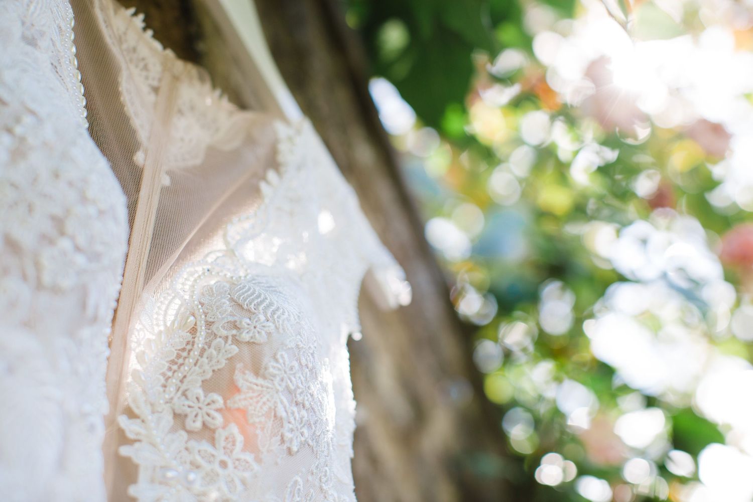Close-up detail of delicate white lace wedding dress hanging outdoors at the Farm at South Cove in Lunenberg with soft bokeh background.