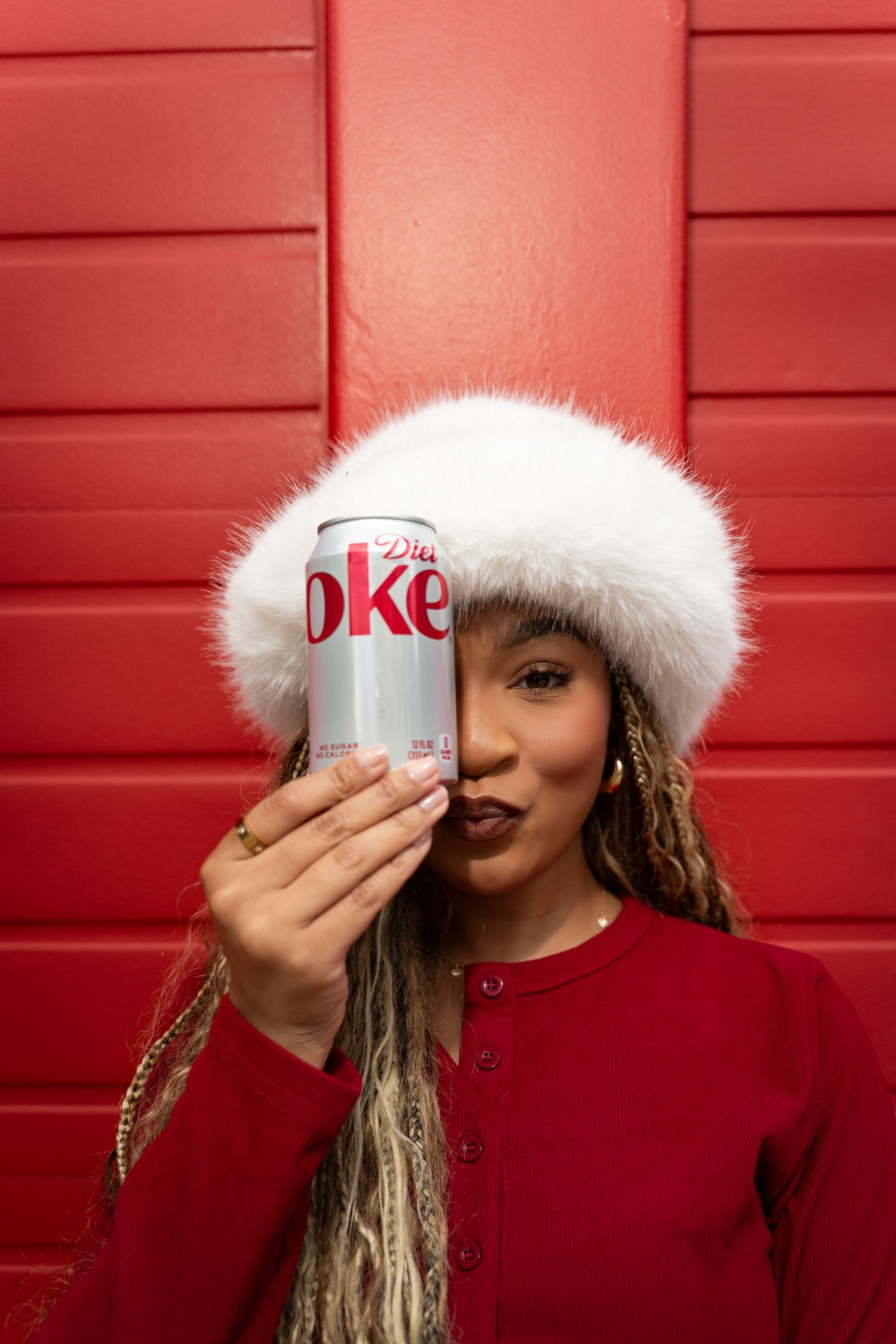 Person in red sweater and white fur hat drinks from a Diet Coke can against a red background in a sequence of photos.