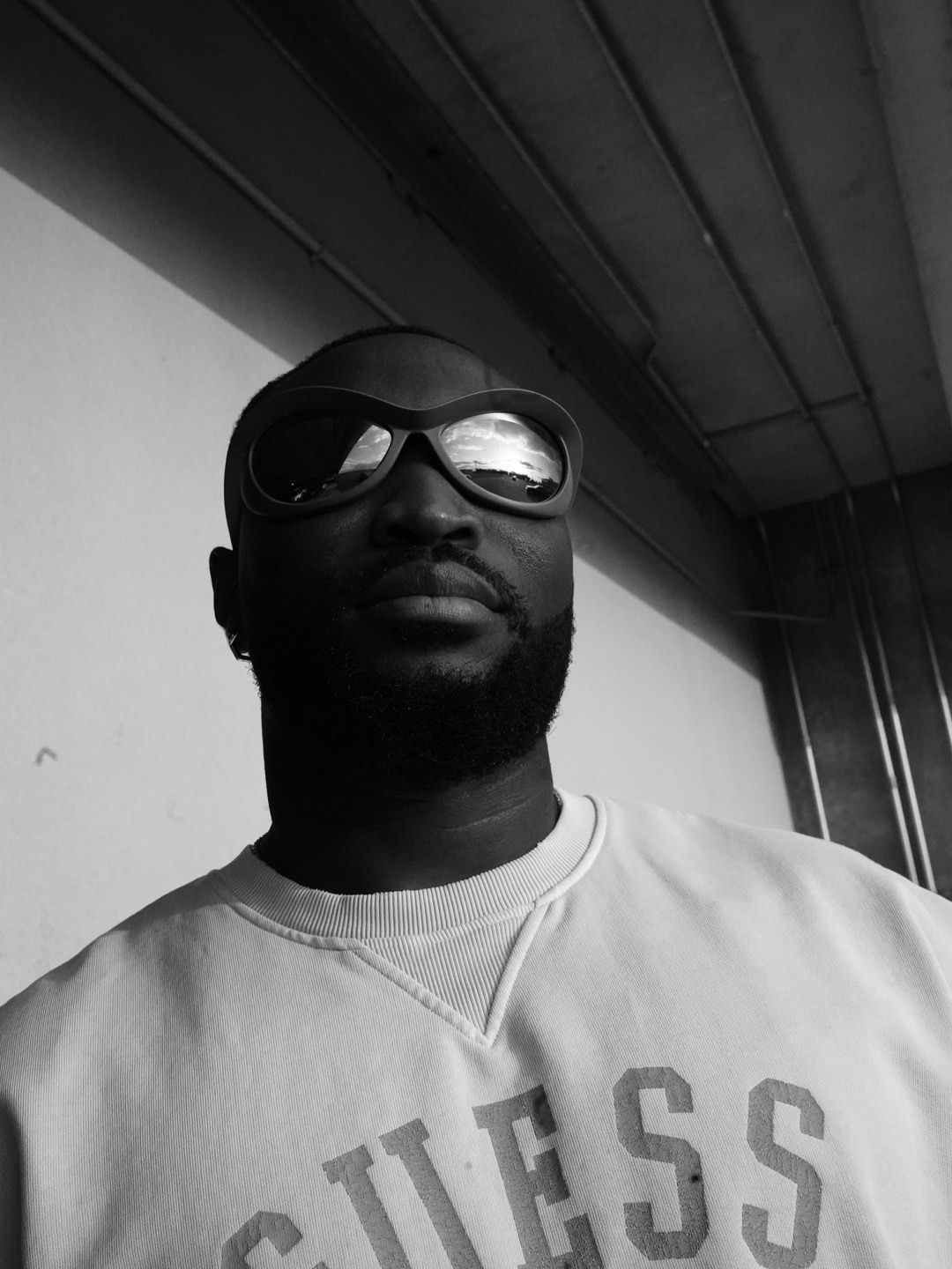 Person wearing sunglasses and white shirt in black and white portrait.