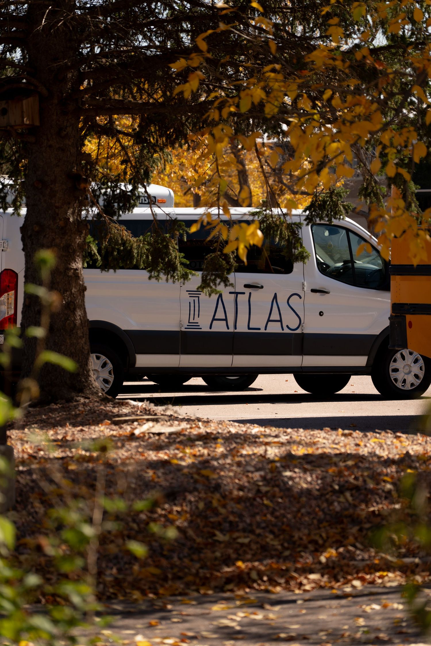 White van with Atlas text visible parked under autumn trees with fallen leaves.