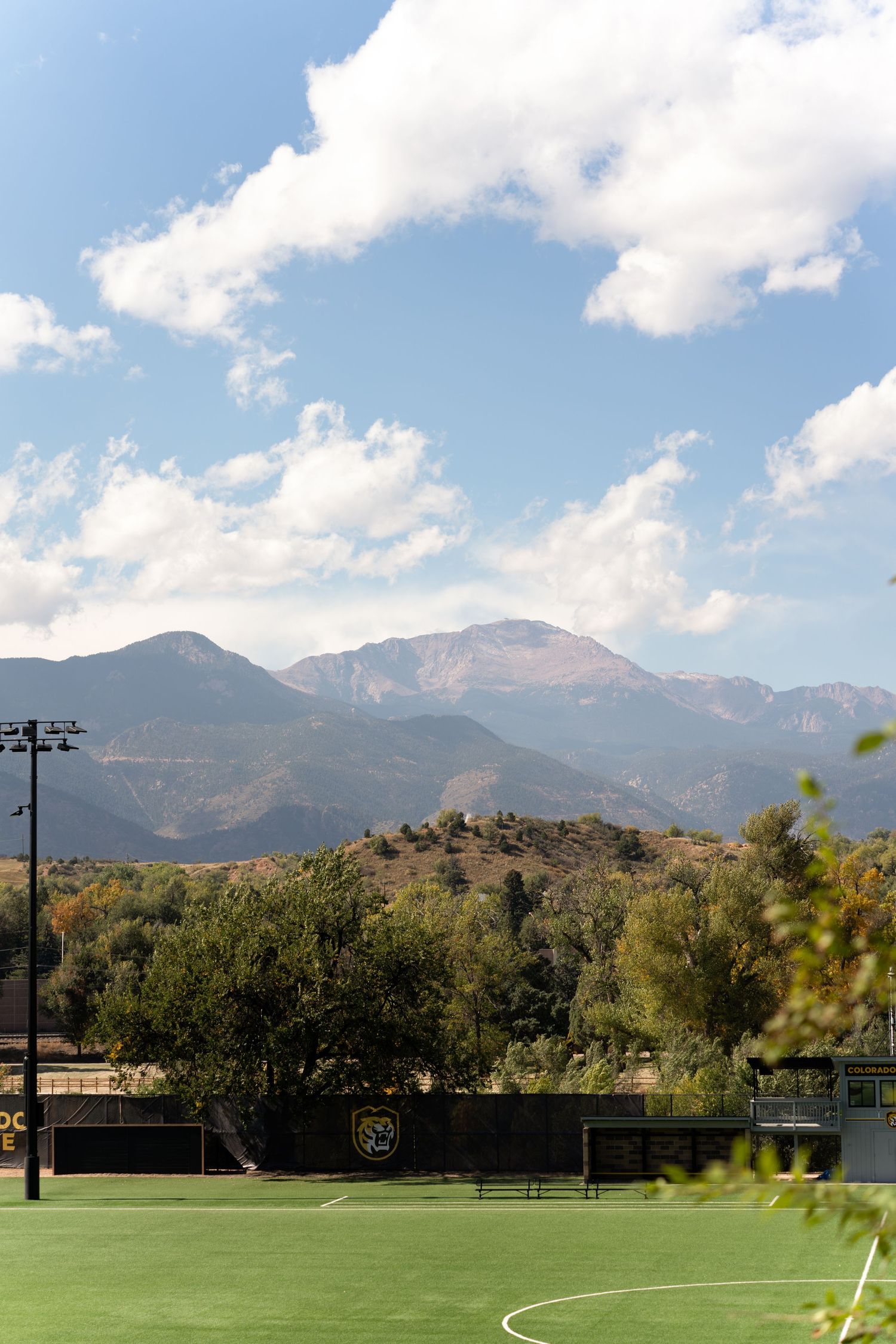 Soccer field with artificial turf surrounded by mountains and blue skies at a sports facility.