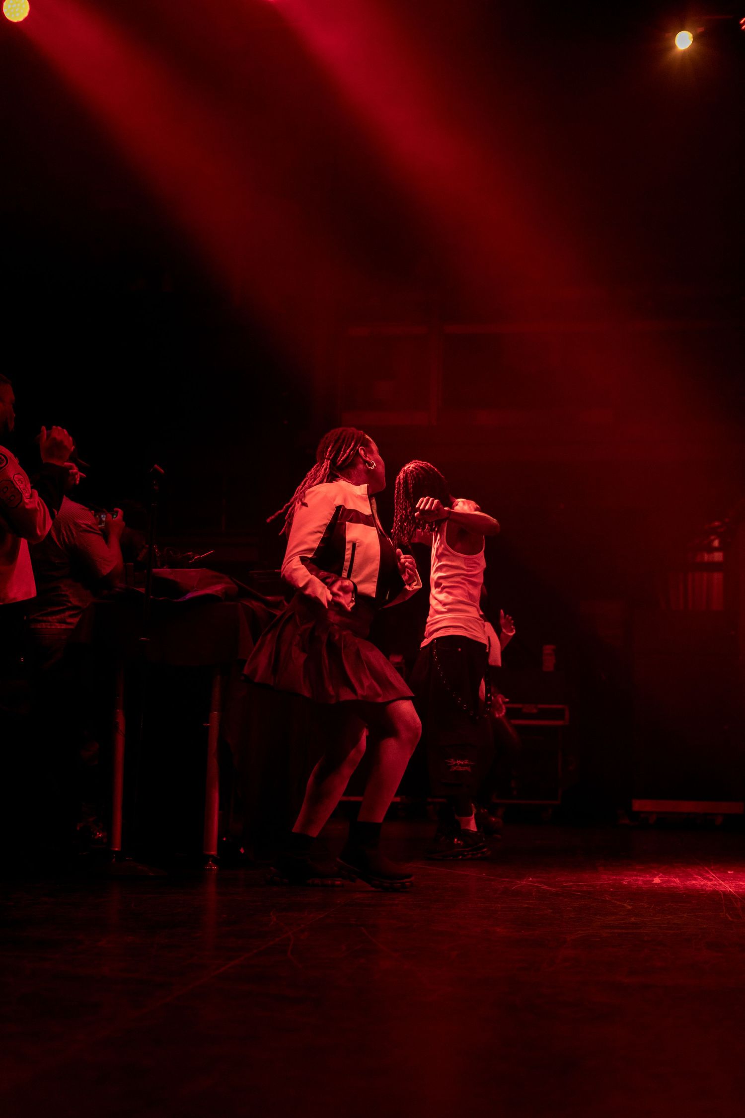 Dancers perform an energetic dance sequence on a dimly lit stage bathed in dramatic red lighting.