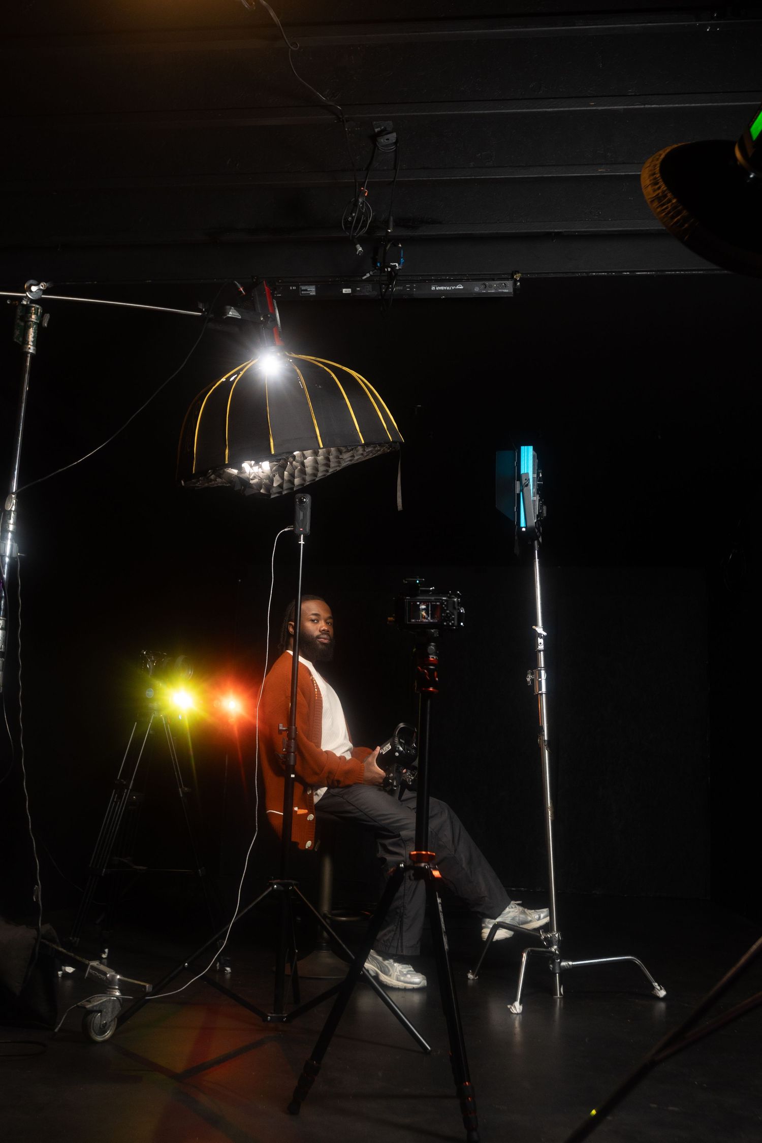 Musician playing guitar in a dark studio setup with professional lighting equipment and microphone stands.