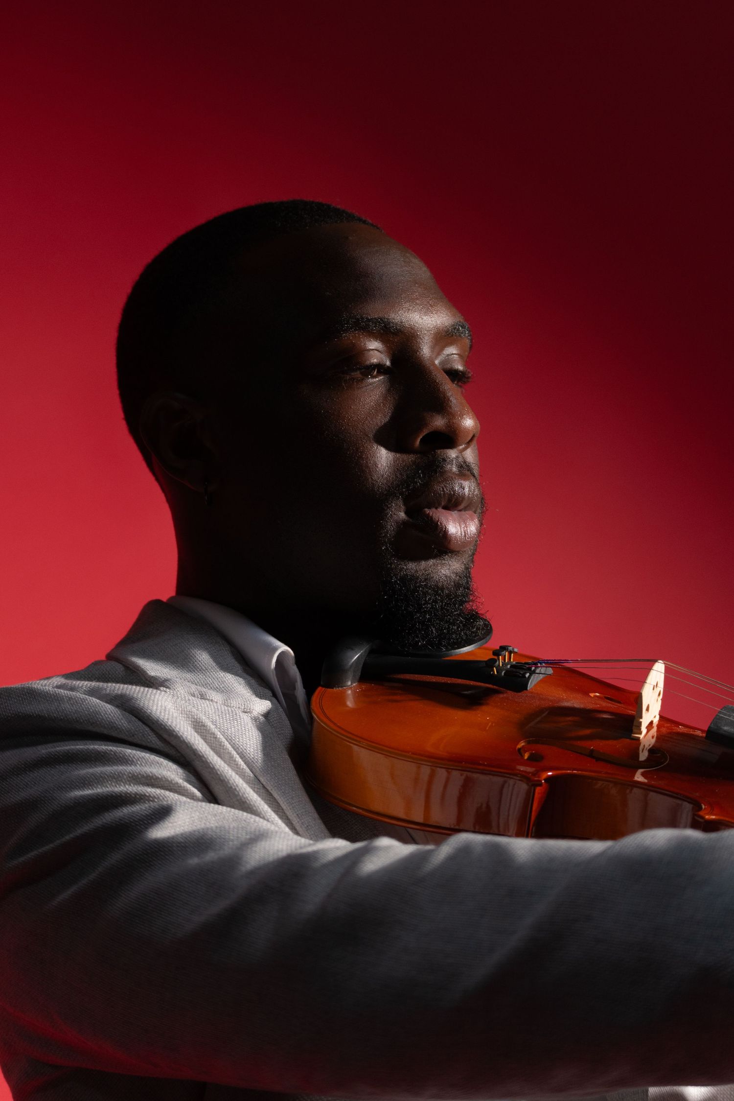 Artistic portrait of musician with violin against dramatic red lighting.