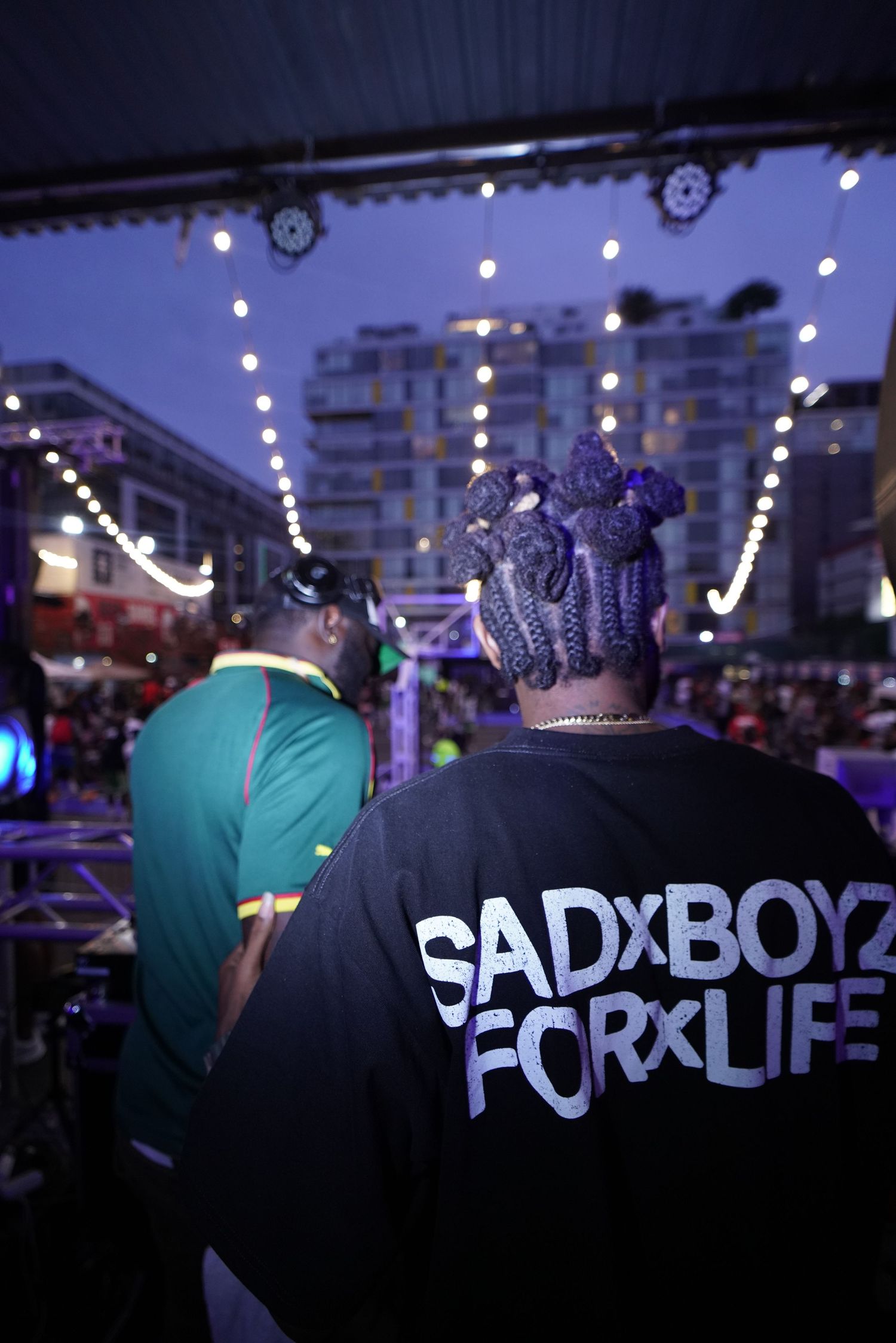 Nighttime crowd scene with illuminated signage and string lights in urban setting.