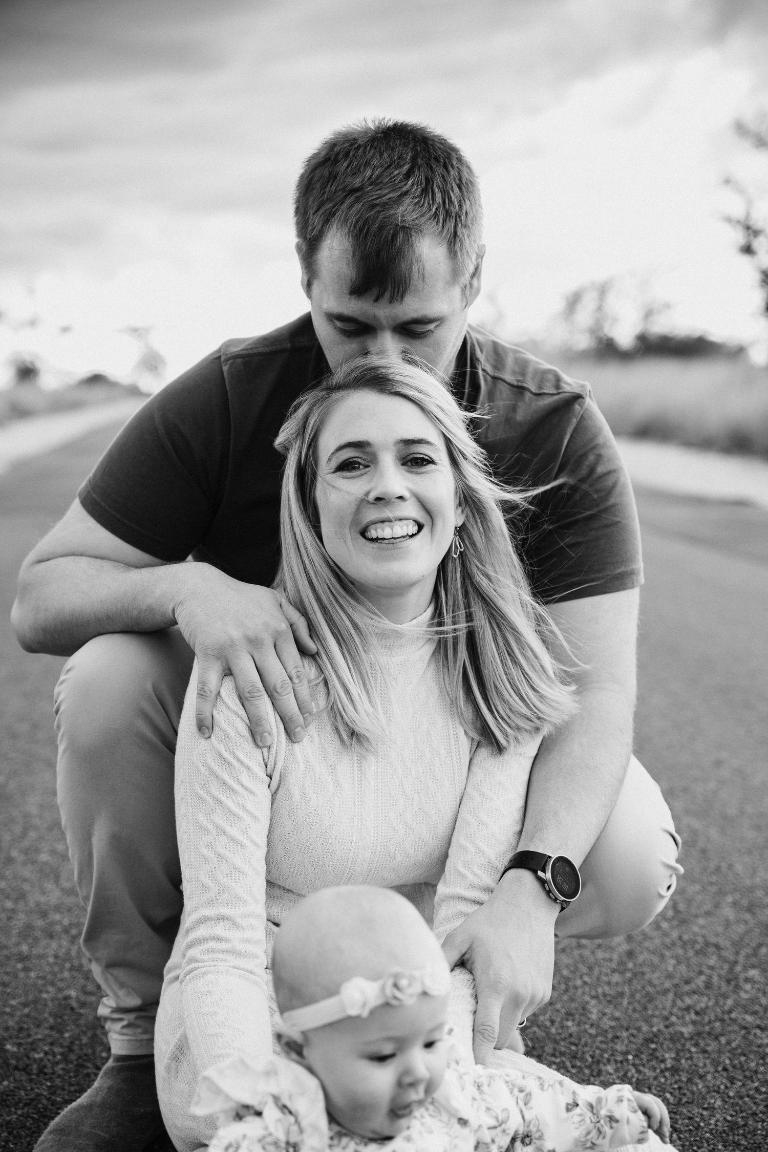A series of black and white photos showing a playful moment between two people laying on grass outdoors.