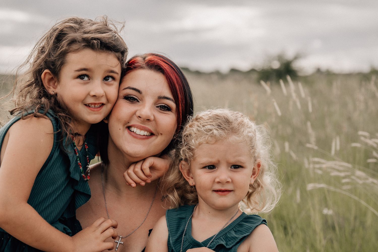 Family portrait taken outdoors in field of tall grass on cloudy day.