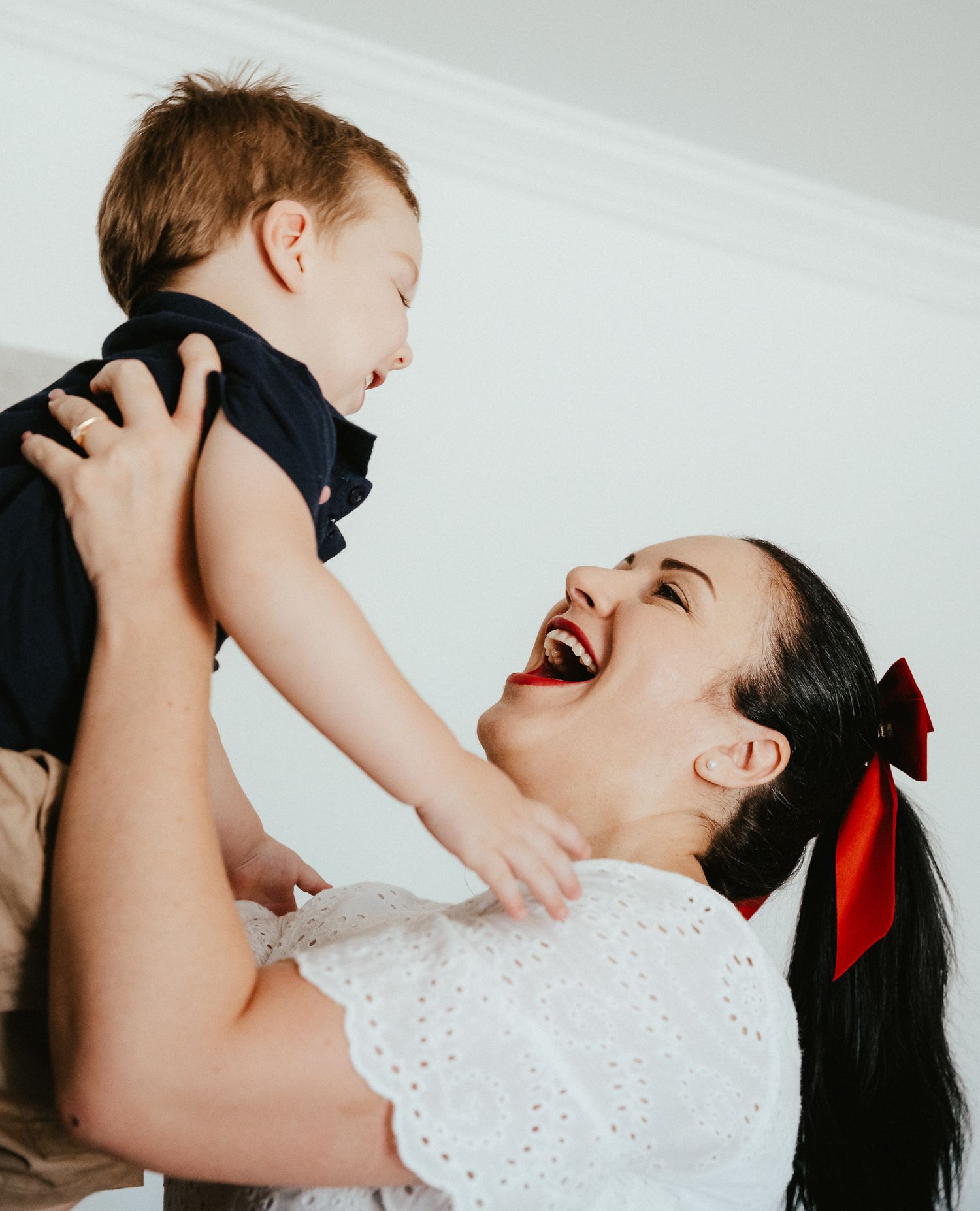 Mother in white dress playfully lifting child while both laugh with joy.
