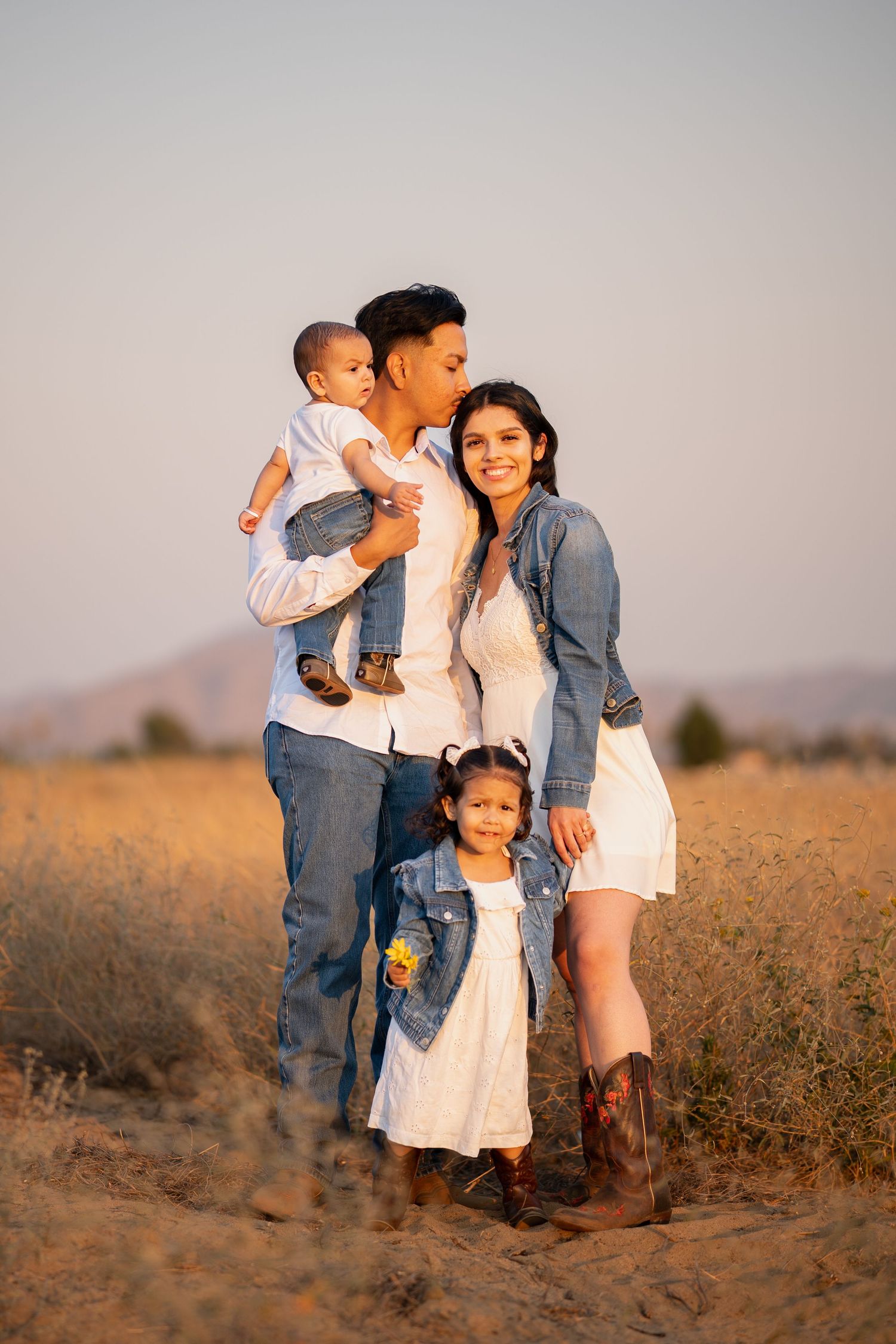 A family shares tender moments together in a golden field at sunset, wearing coordinated casual outfits.