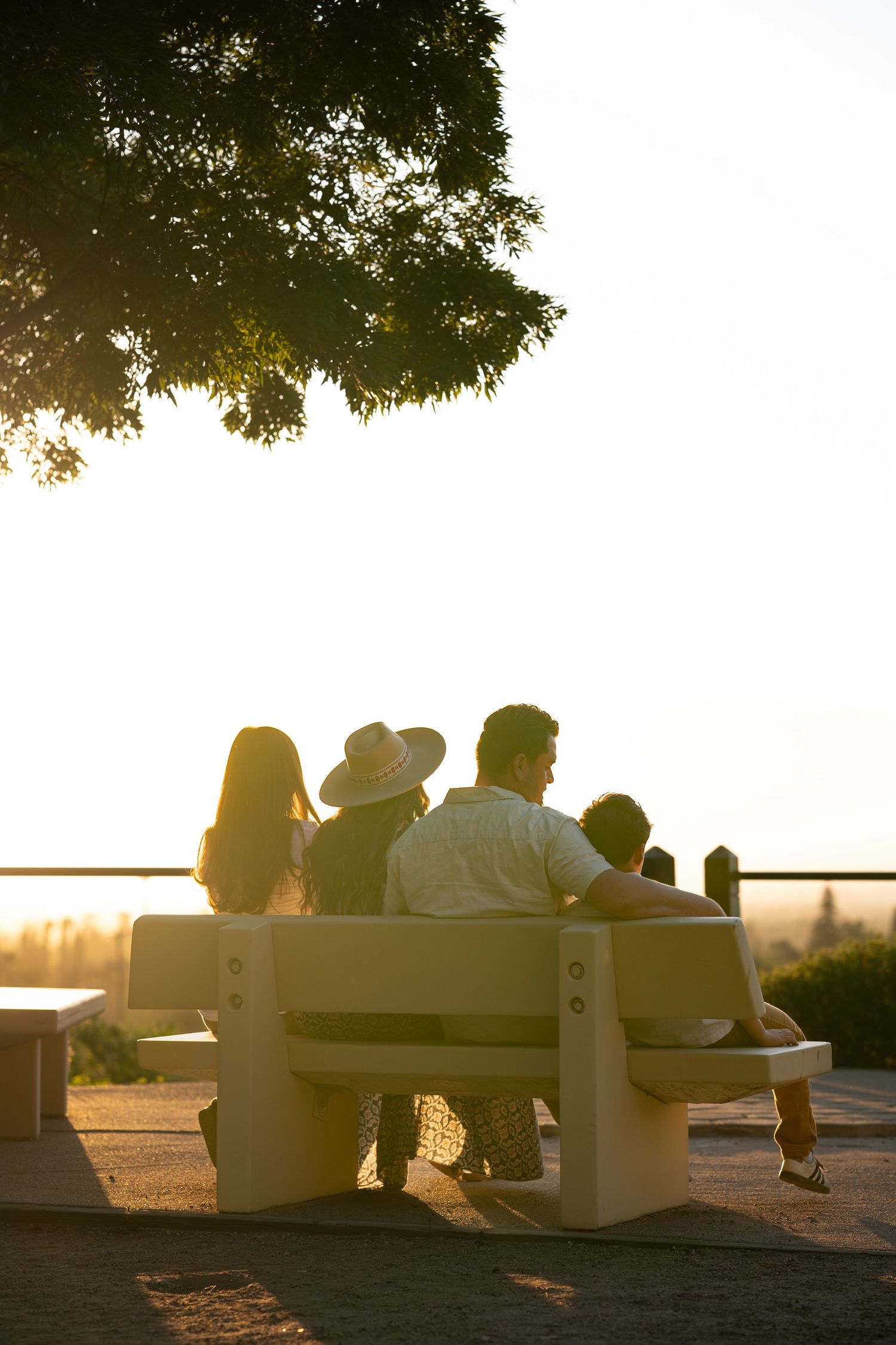 People silhouetted against sunset sky sit together on benches overlooking water.