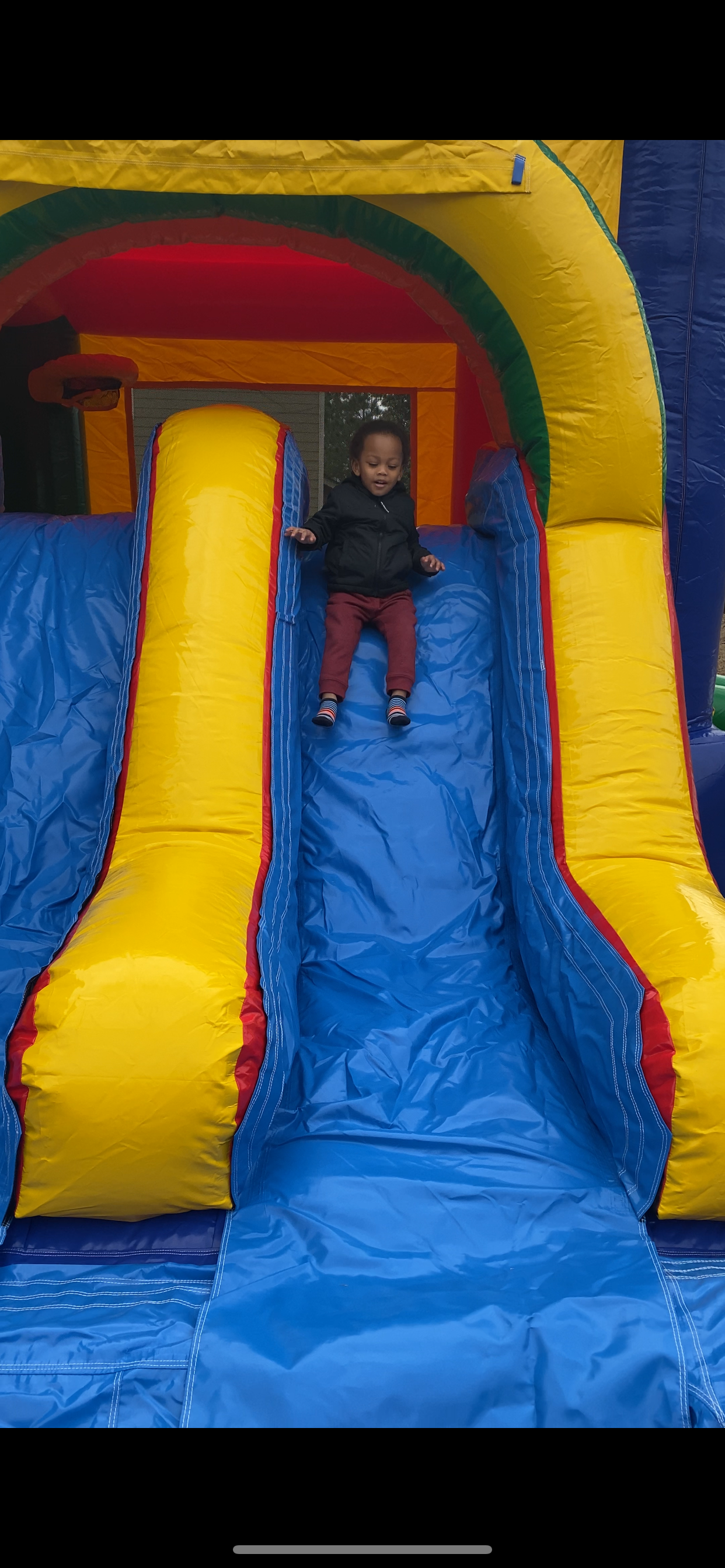 A colorful inflatable bounce house with blue slide and yellow side rails being enjoyed by a small child.