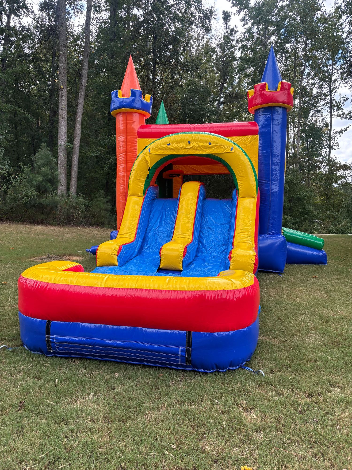 Colorful inflatable bounce house with slide and castle features photographed from multiple angles on a grassy hillside.