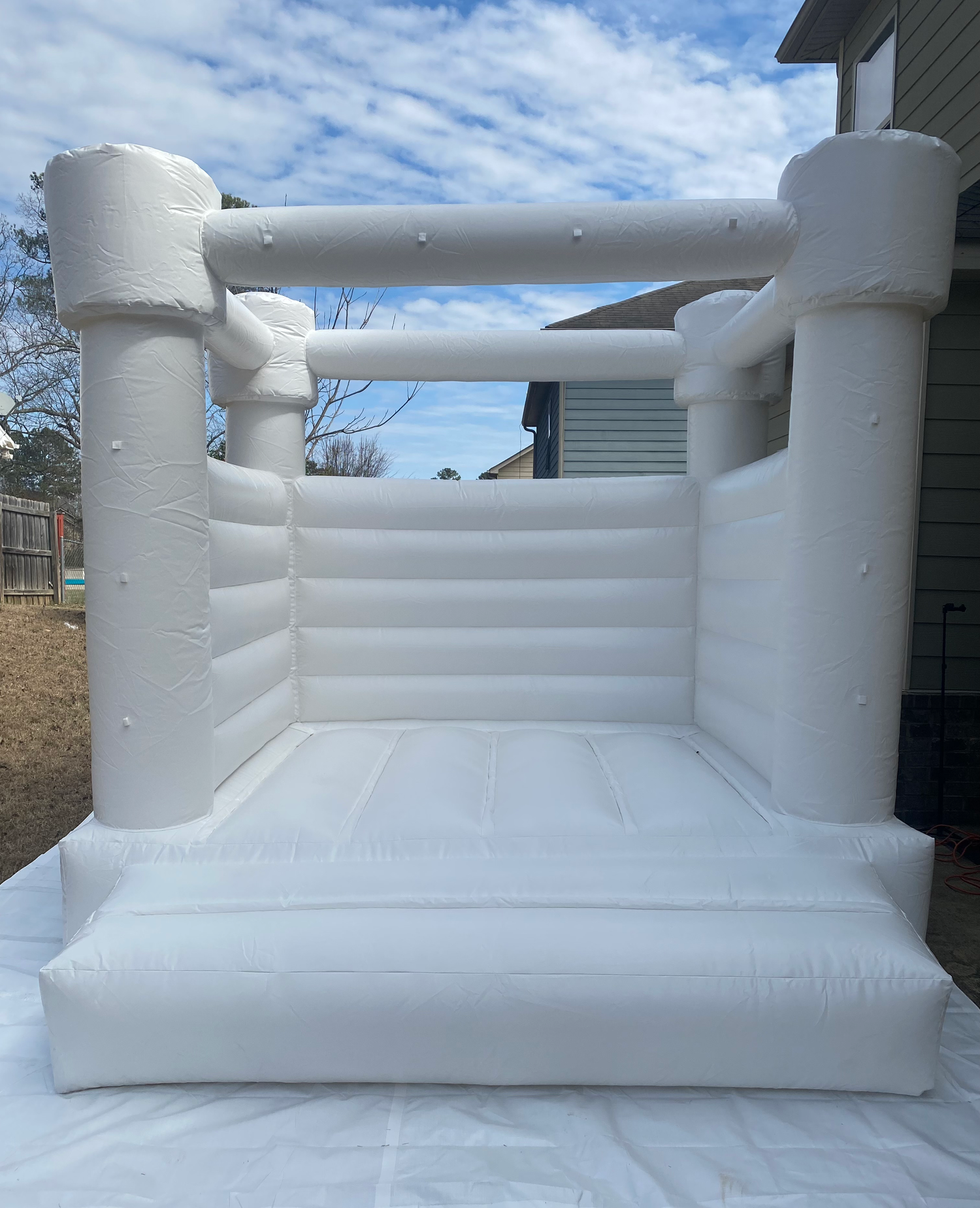 White inflatable bounce castle with pillars and padded floor against blue sky background.