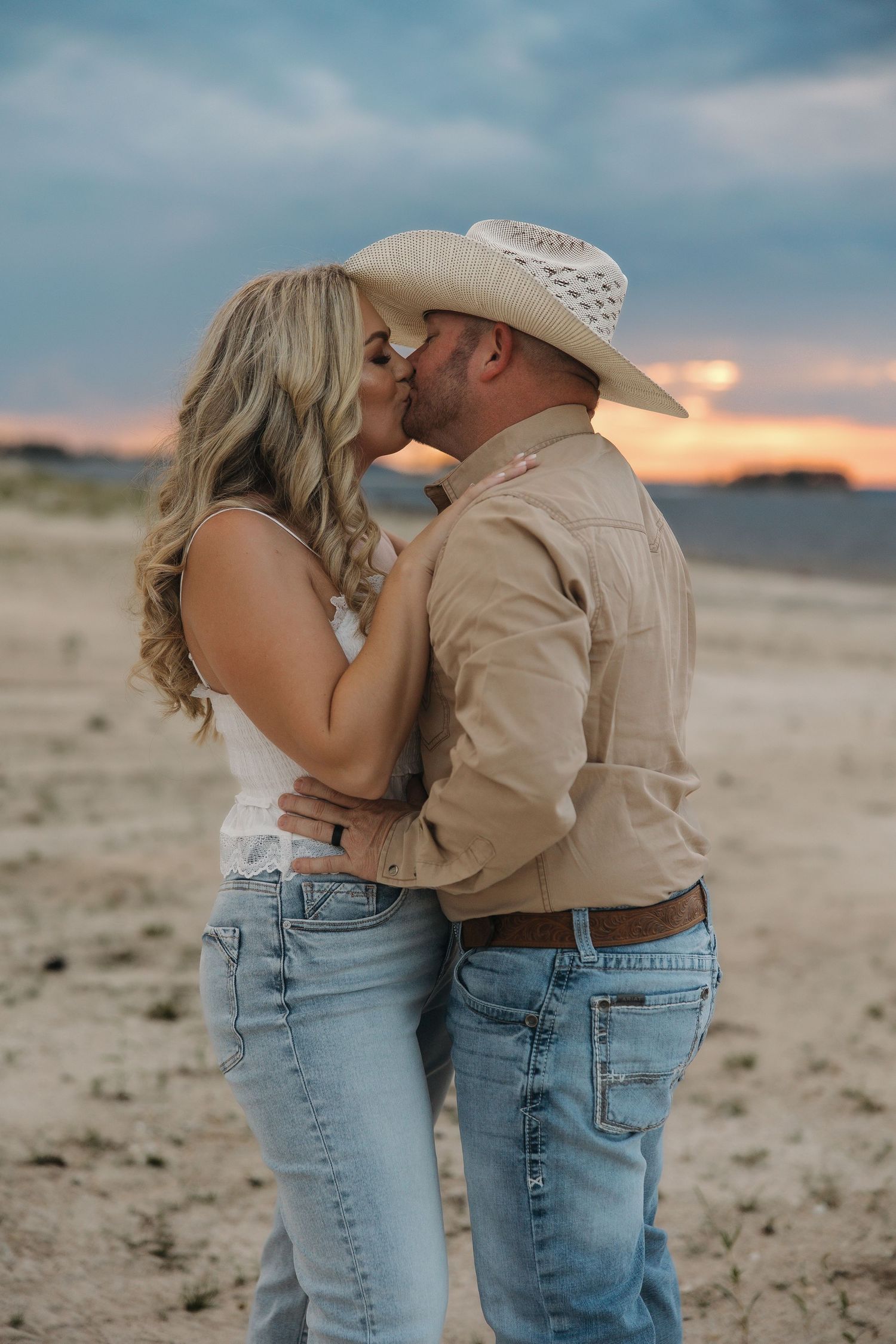A romantic couple shares an intimate moment at sunset in western attire against a desert background.