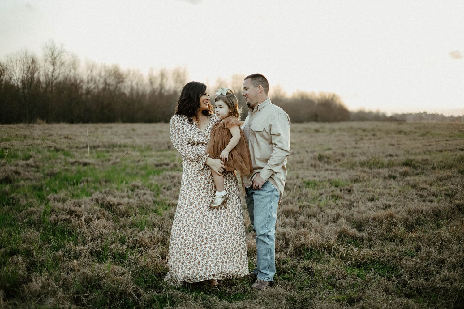 A couple shares an intimate moment in a polka dot dress and jeans while standing in a golden field at sunset.
