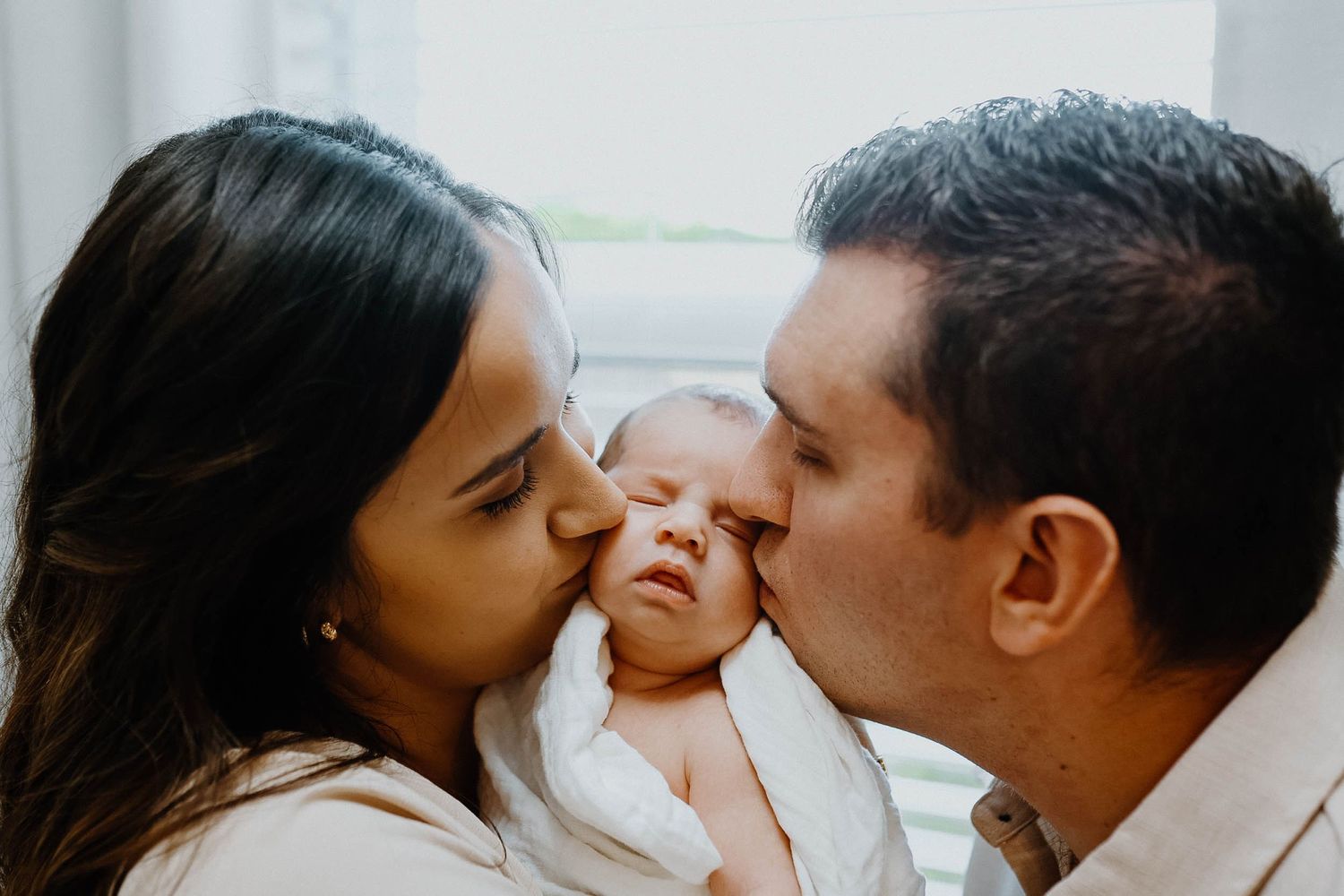 Parents shower their newborn baby with kisses in an intimate family portrait.