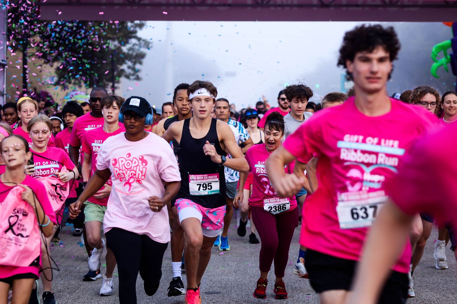 Participants wearing pink shirts running together in a charity race or marathon event on a cloudy day.