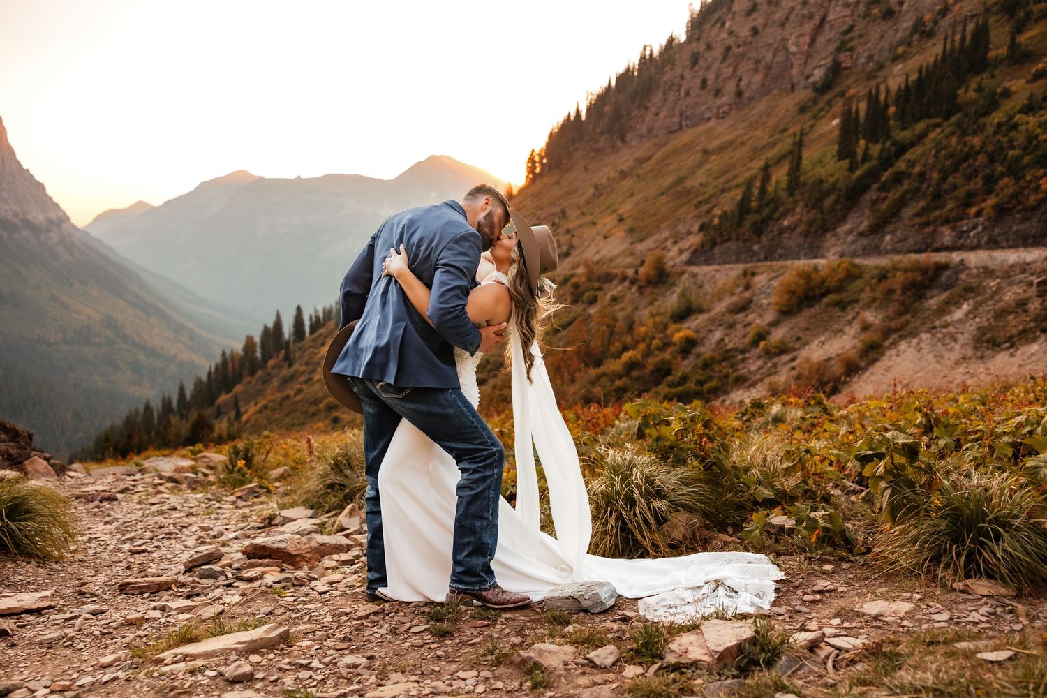 A couple shares a romantic moment against a stunning mountain backdrop during their wedding photoshoot at sunset.