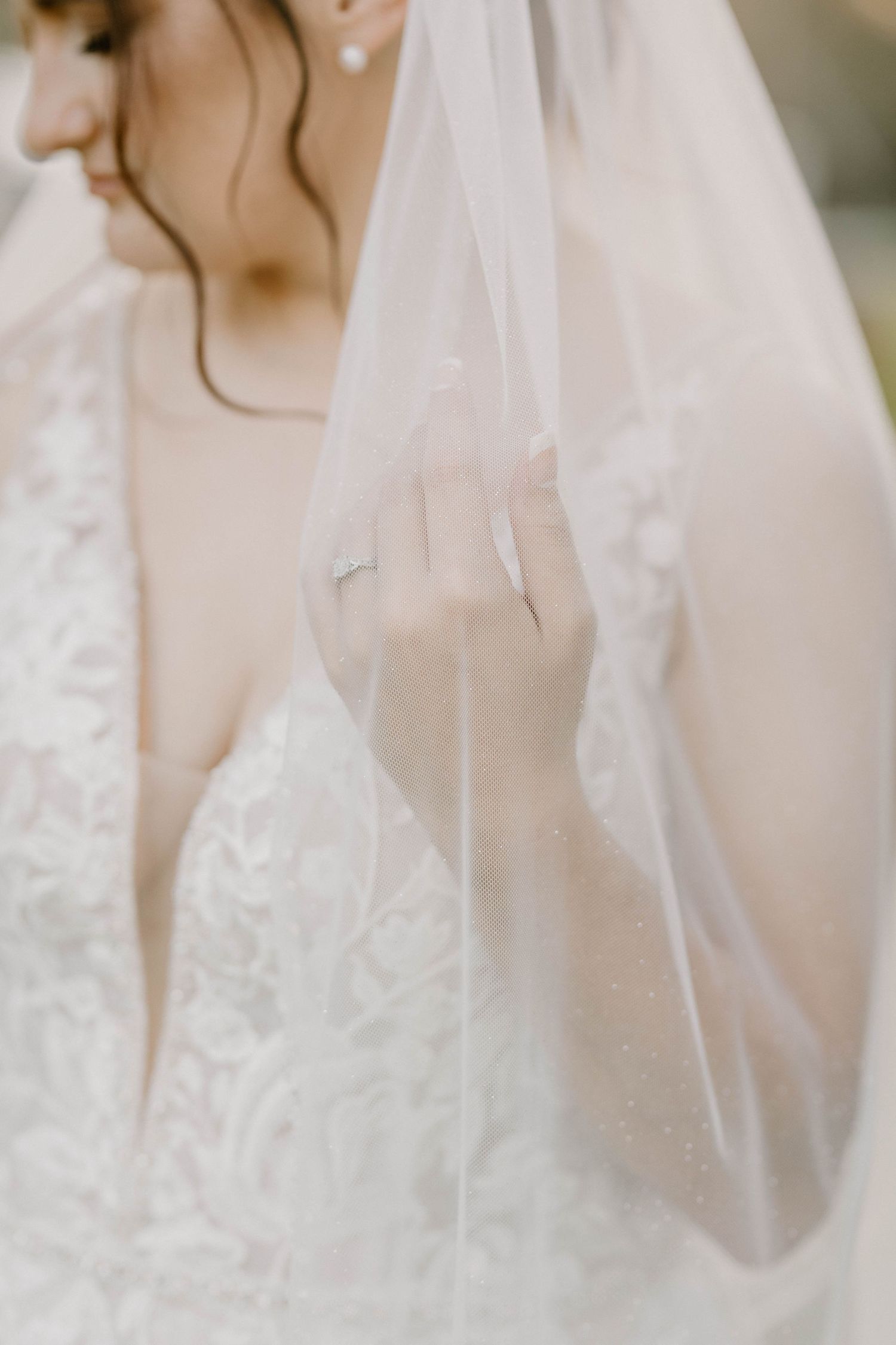 A delicate sheer white wedding veil drapes softly over a lace bridal gown in an ethereal close-up shot.