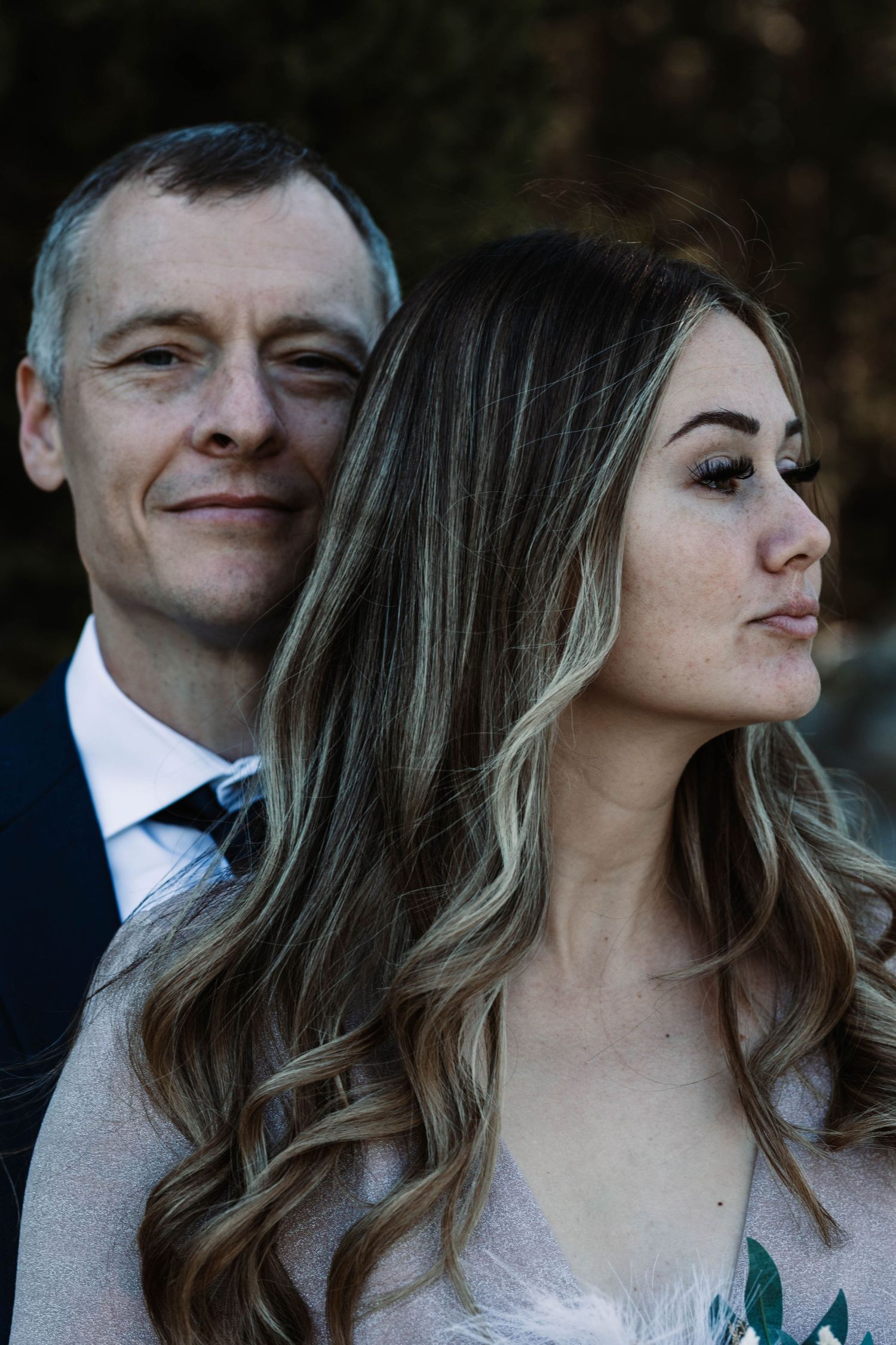 Wedding portrait of a couple in formal attire with the bride wearing a white dress and having long wavy highlighted hair.